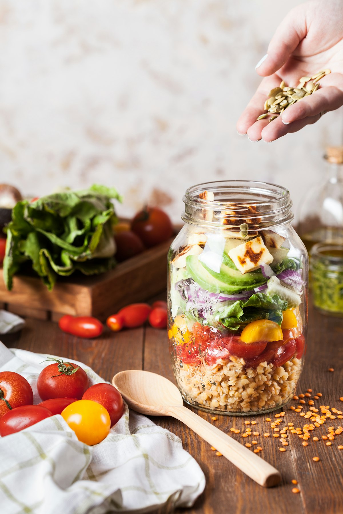 Salade en bocal avec légumes frais, grains et fromage, main ajoutant des graines, style sain et rustique.