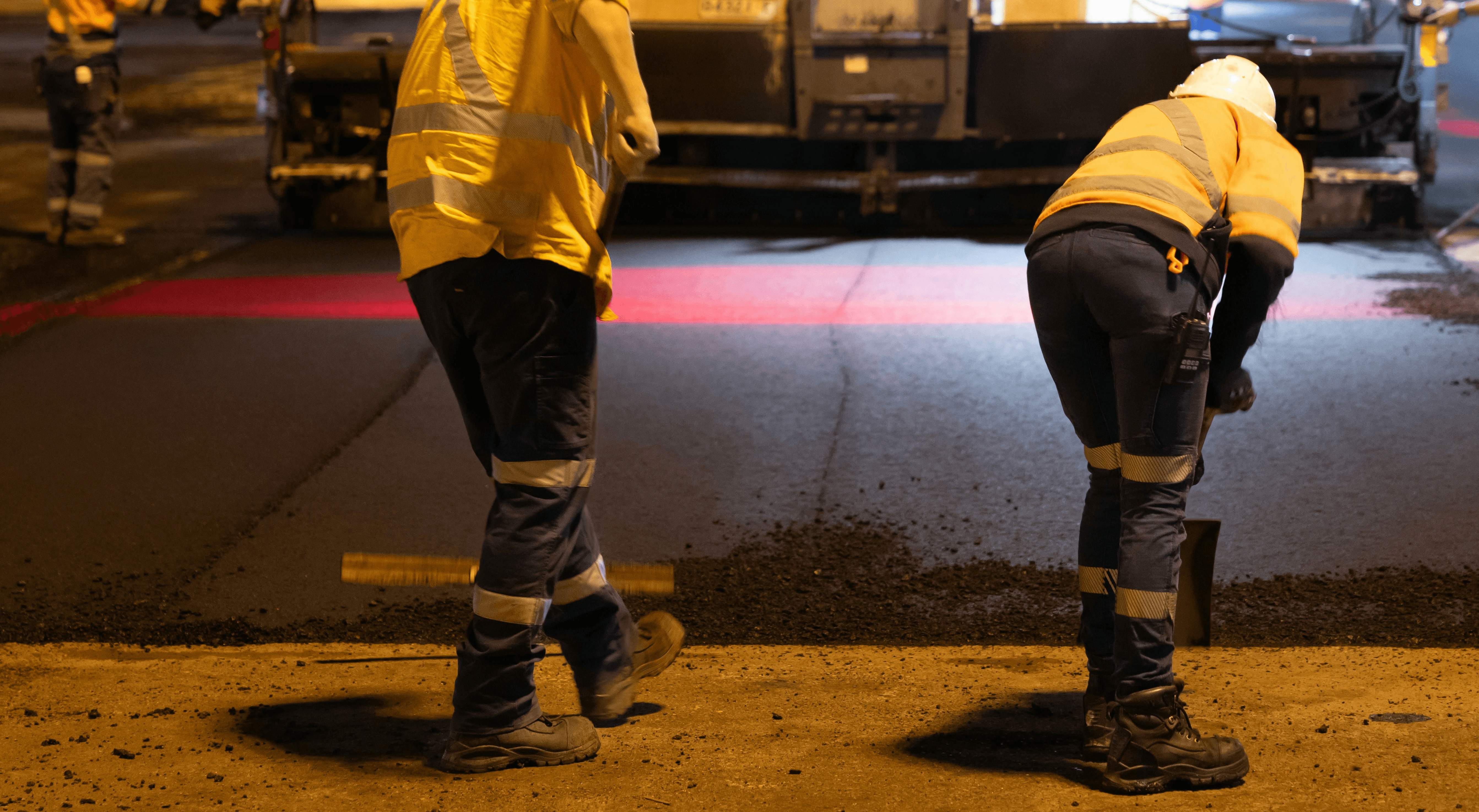 Travailleurs déneigeant une route la nuit avec des équipements de sécurité et éclairage de chantier.