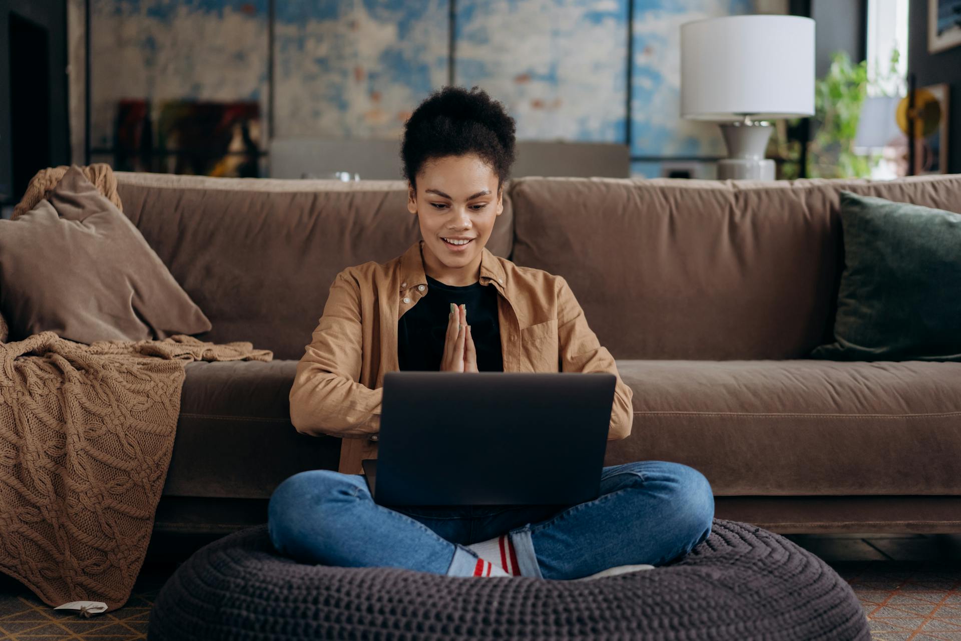 A woman engaging in online therapy. Sitting on a safa with a laptop resting on her legs