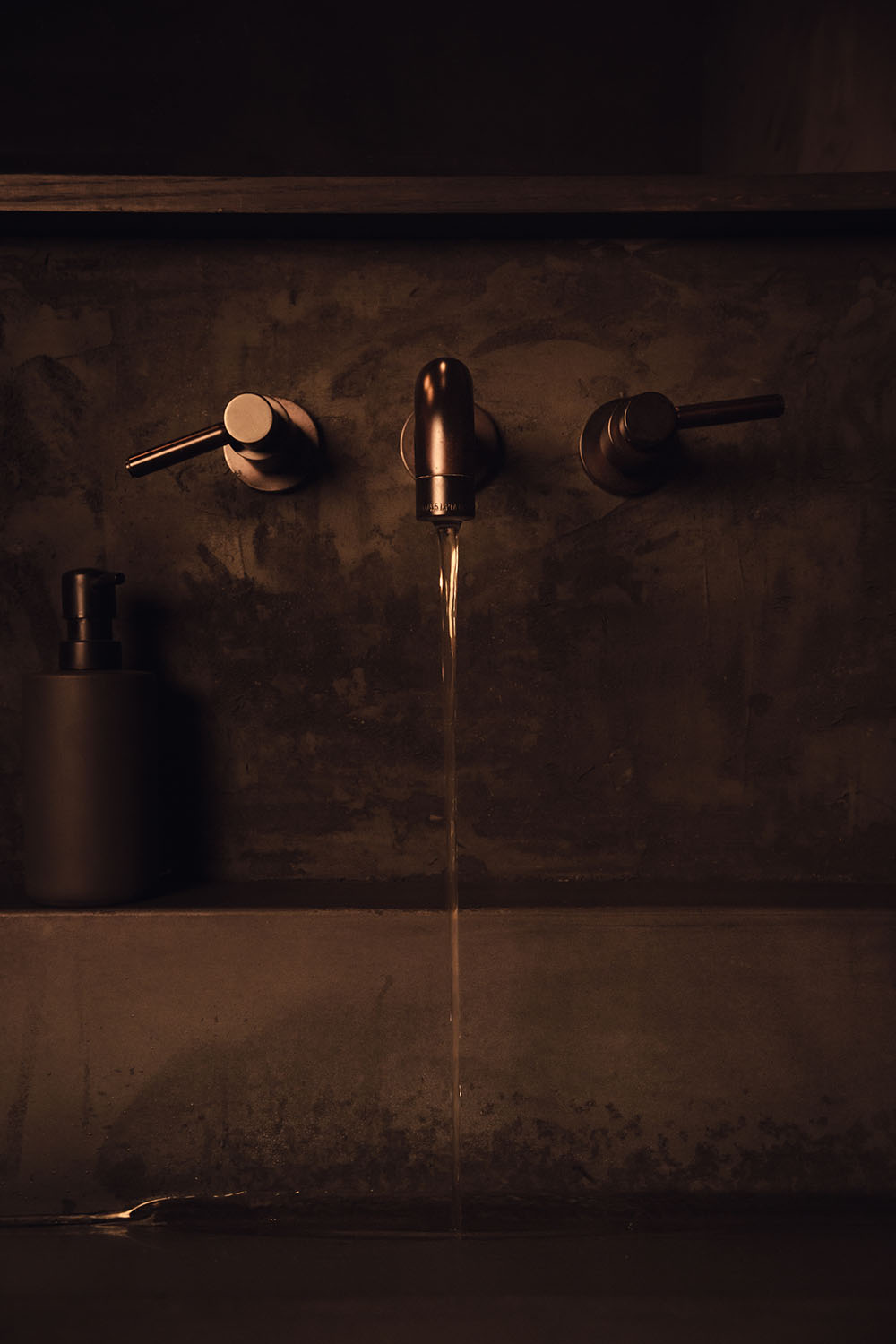 A faucet is in the on position and a laminer flow of water runs down to the basin of the sink in the washroom of Particle Studio in Seattle, WA.