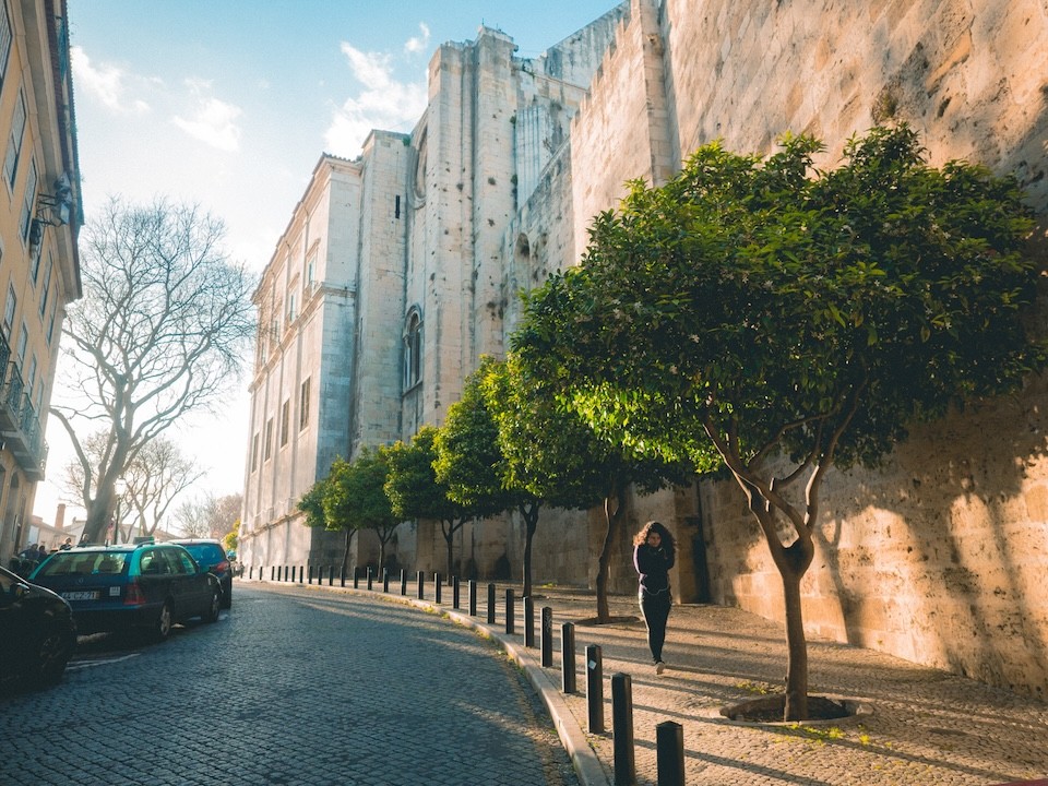 Street photography of a woman walking under the trees and next to a historical building during the golden hour