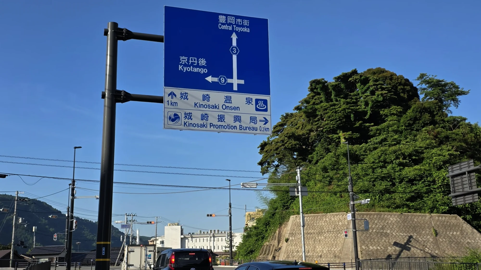 A blue Japanese road sign pointing to Kinosaki Onsen one kilometre ahead.