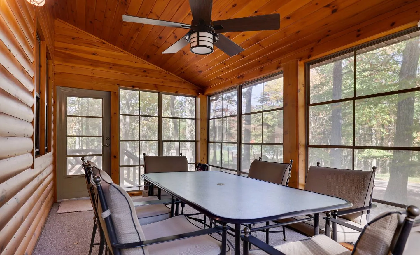 Enclosed porch with six-seat dining table, ceiling fan and window walls at Barefoot Bungalow
