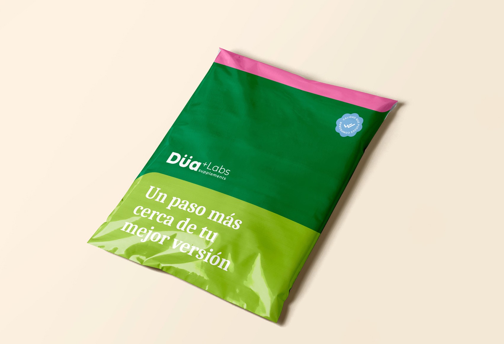 A green and pink Dua Labs packaging bag is displayed against a light background, featuring Spanish text that reads "Un paso más cerca de tu mejor versión" alongside a blue certification badge.