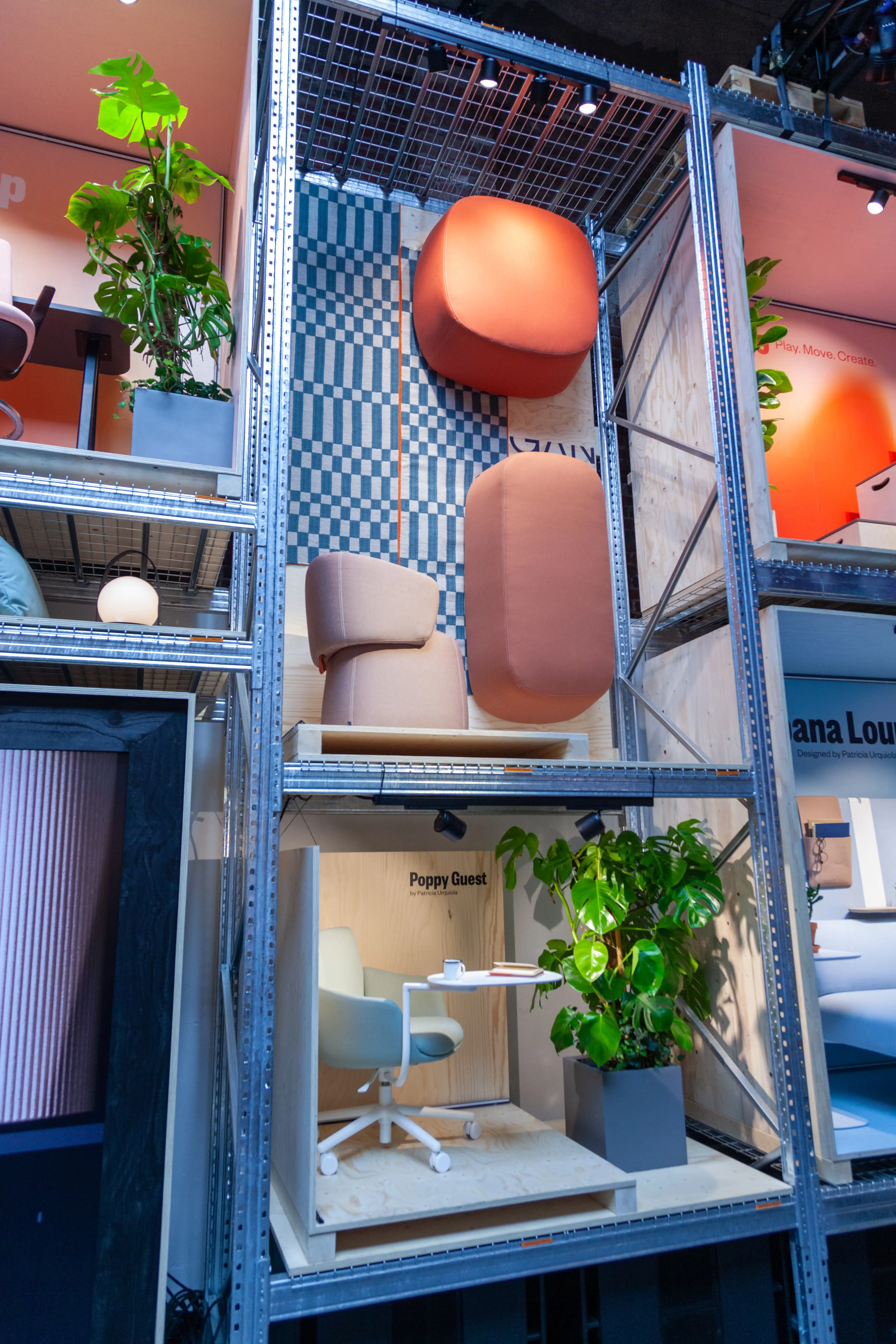 Terracotta poufs and seating modules in front of checkered wallpaper inside the shelving display at the Haworth booth.