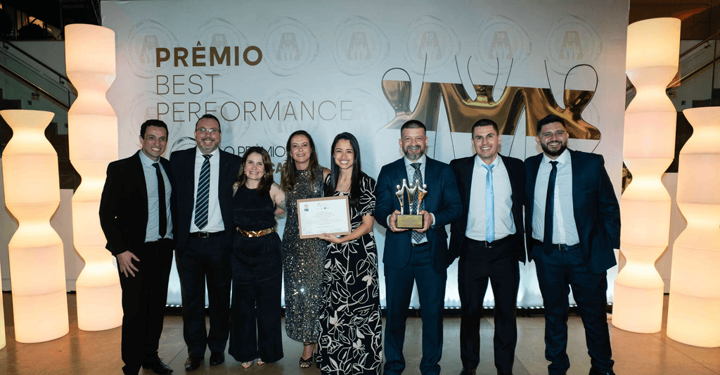 Executivos da BELLINATI PEREZ posando com troféu ouro e certificado no palco do Prêmio Best Performance 2025