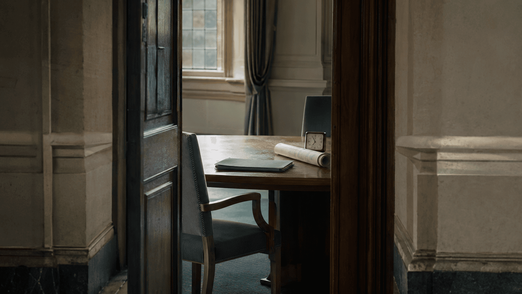 An open civic meeting-room doorway with a prepared folder, rolled plan and clock on the table