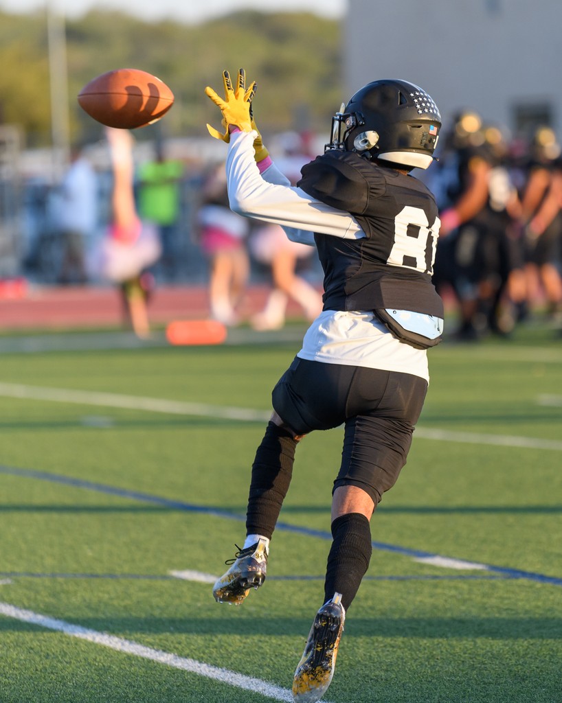 High school football player making a mid-air catch during a game, demonstrating athleticism and precision on the field.