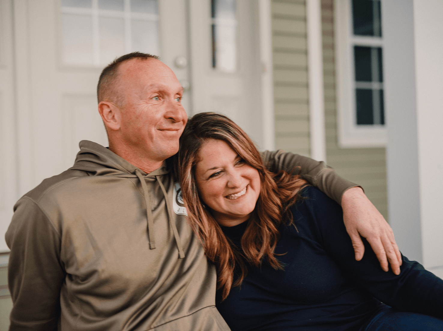 A smiling couple sits on their porch together.
