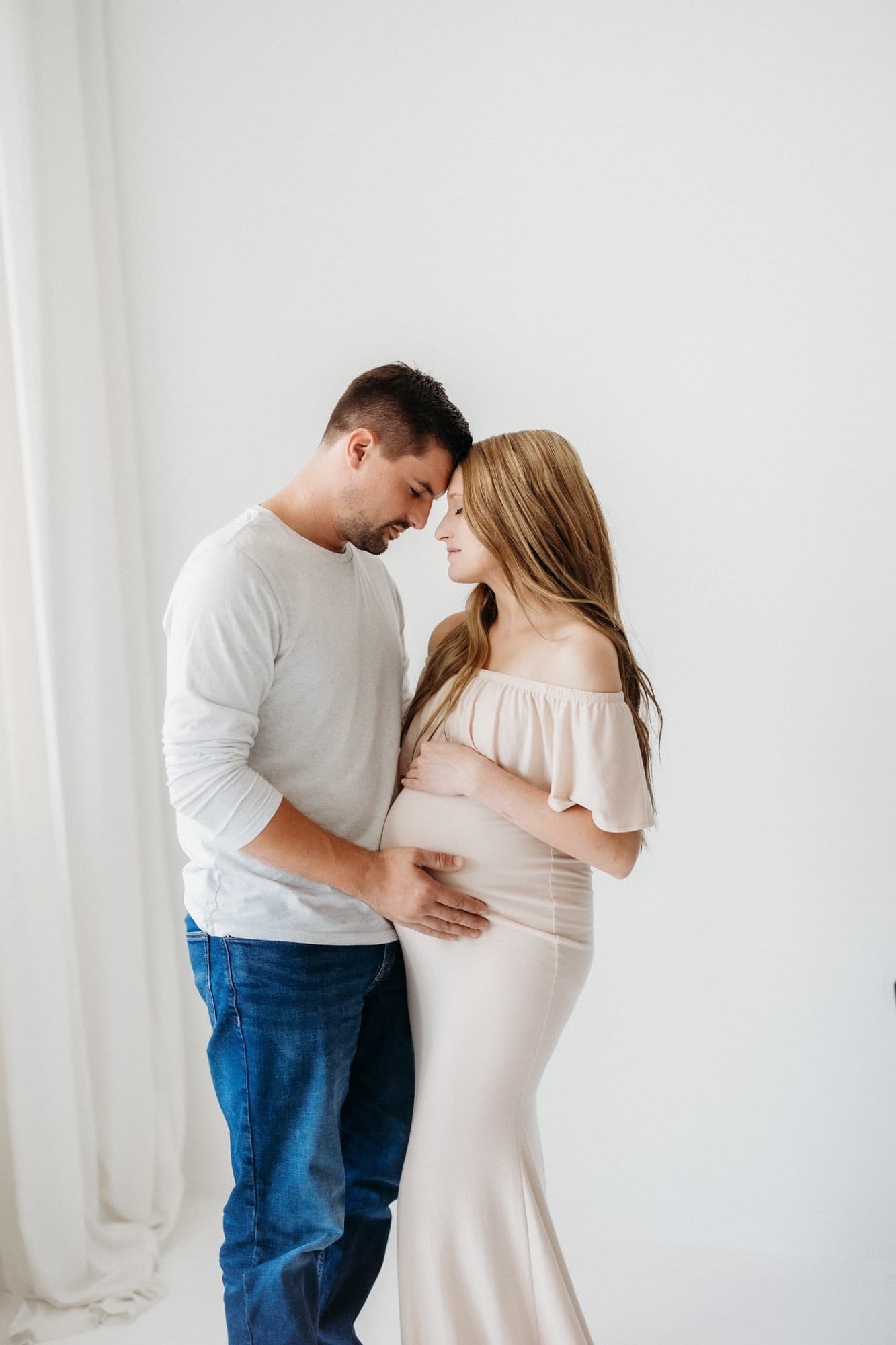 A couple shares a tender moment, foreheads touching, during a maternity photoshoot at Revelator Studio in Shreveport, captured in natural light.