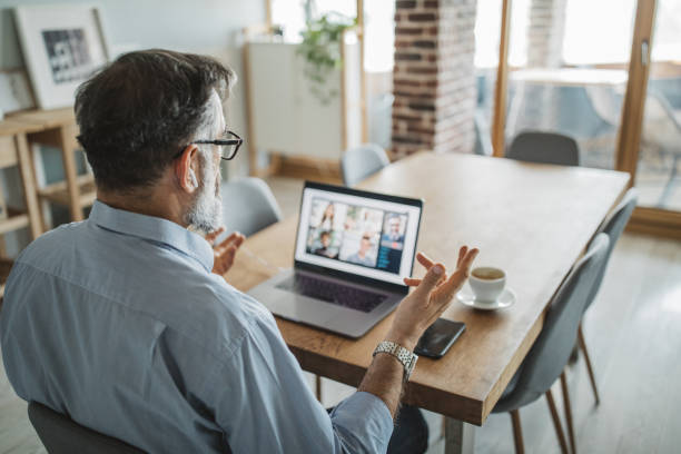 Meeting remoto in ufficio moderno: professionista in videoconferenza su laptop con colleghi, lavoro ibrido e smart working.