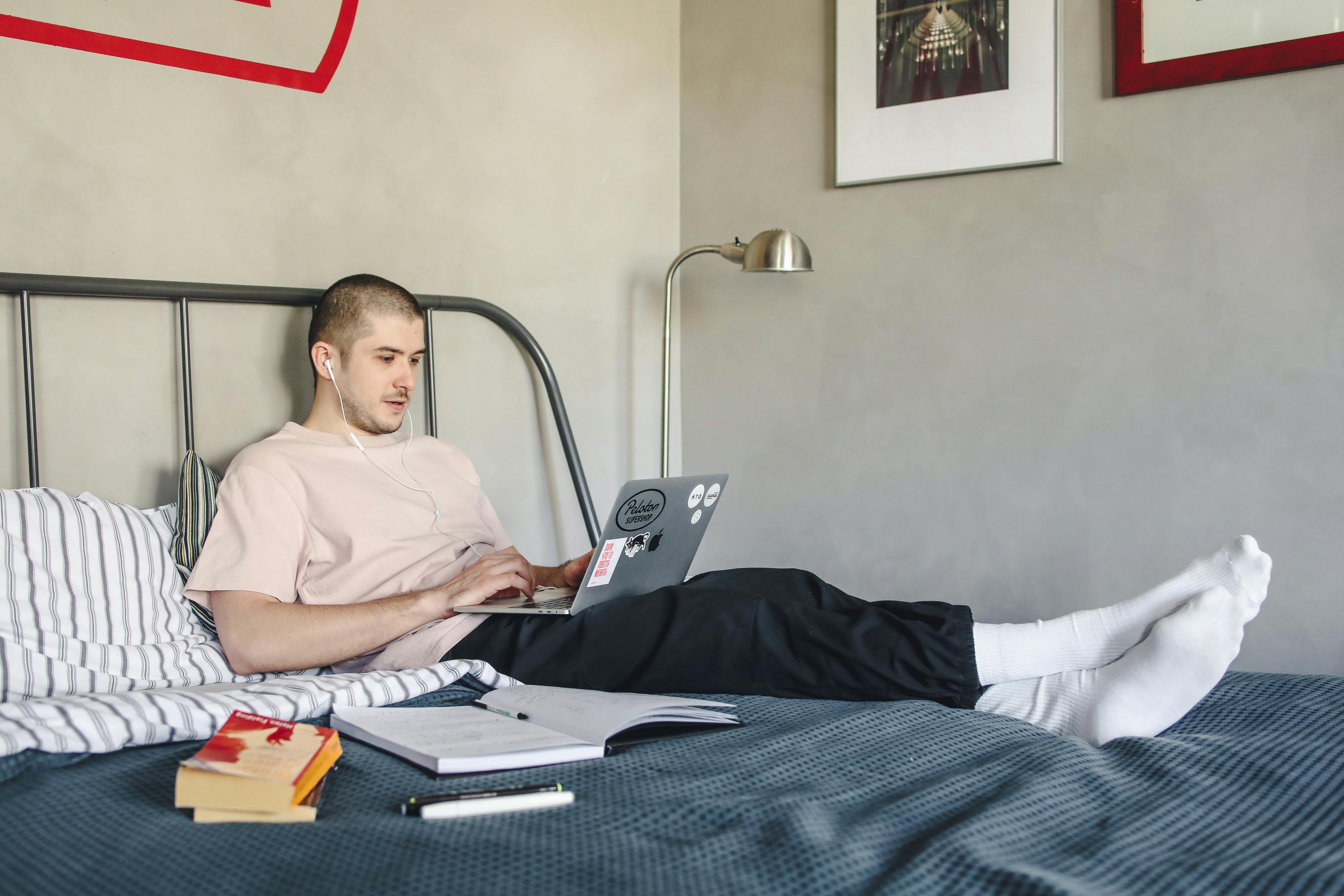 Giovane che segue una lezione online dal proprio letto, simbolo di apprendimento flessibile e crescita personale attraverso percorsi di coaching e formazione digitale.