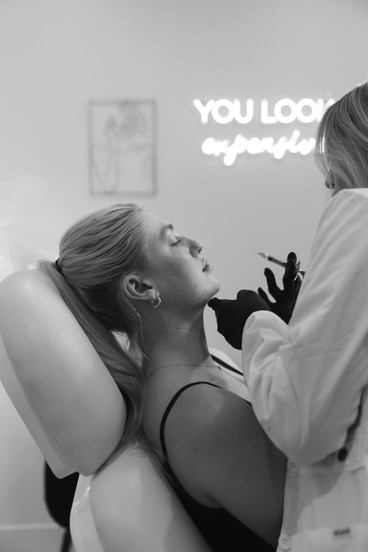 A woman lying on a massage bed, illuminated by soft sunlight streaming through a nearby window. A lush green plant in the background enhances the peaceful and rejuvenating ambiance.