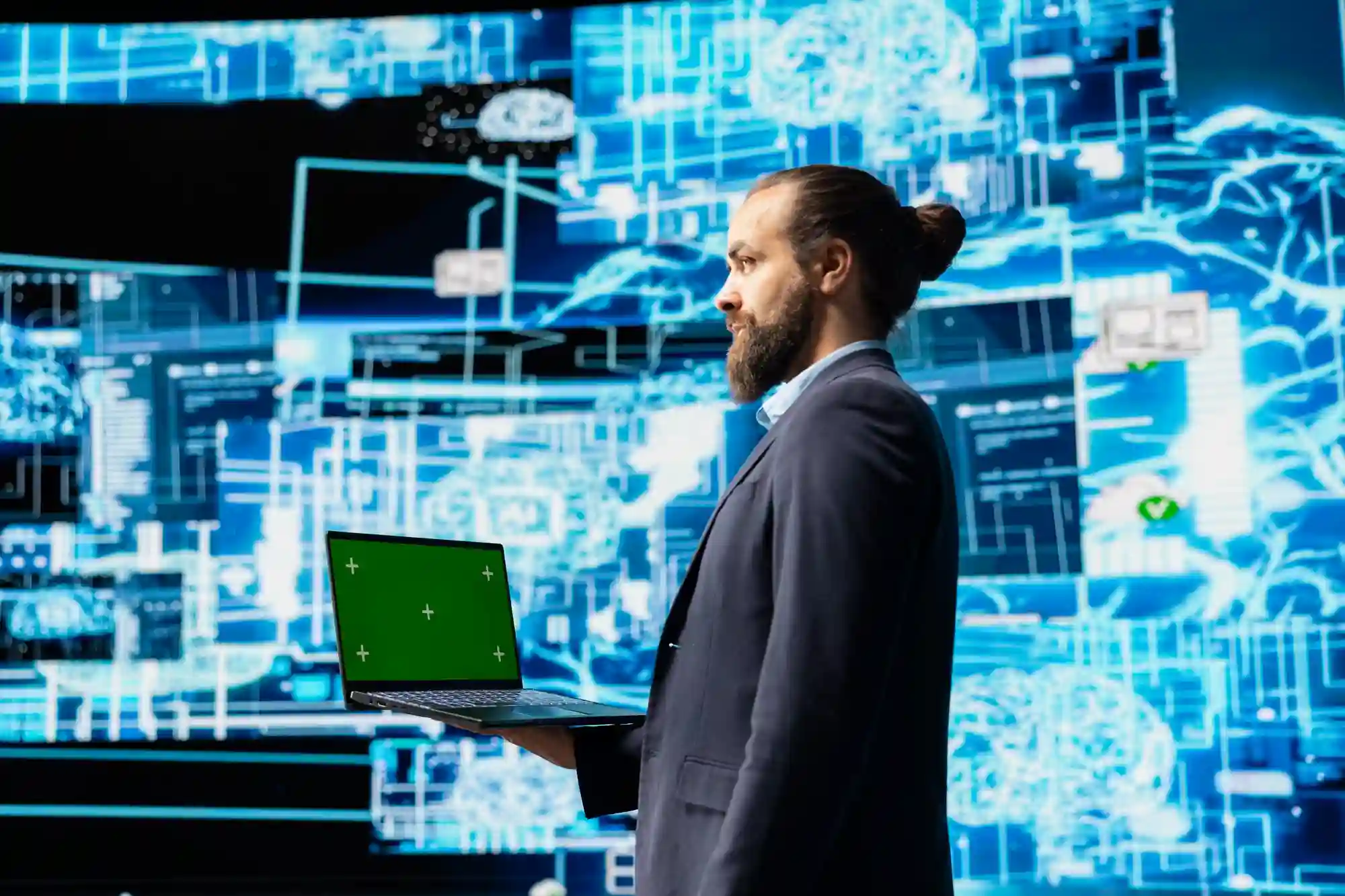 A businessman with a laptop standing before a digital data screen, symbolizing advanced technological integration in business.
