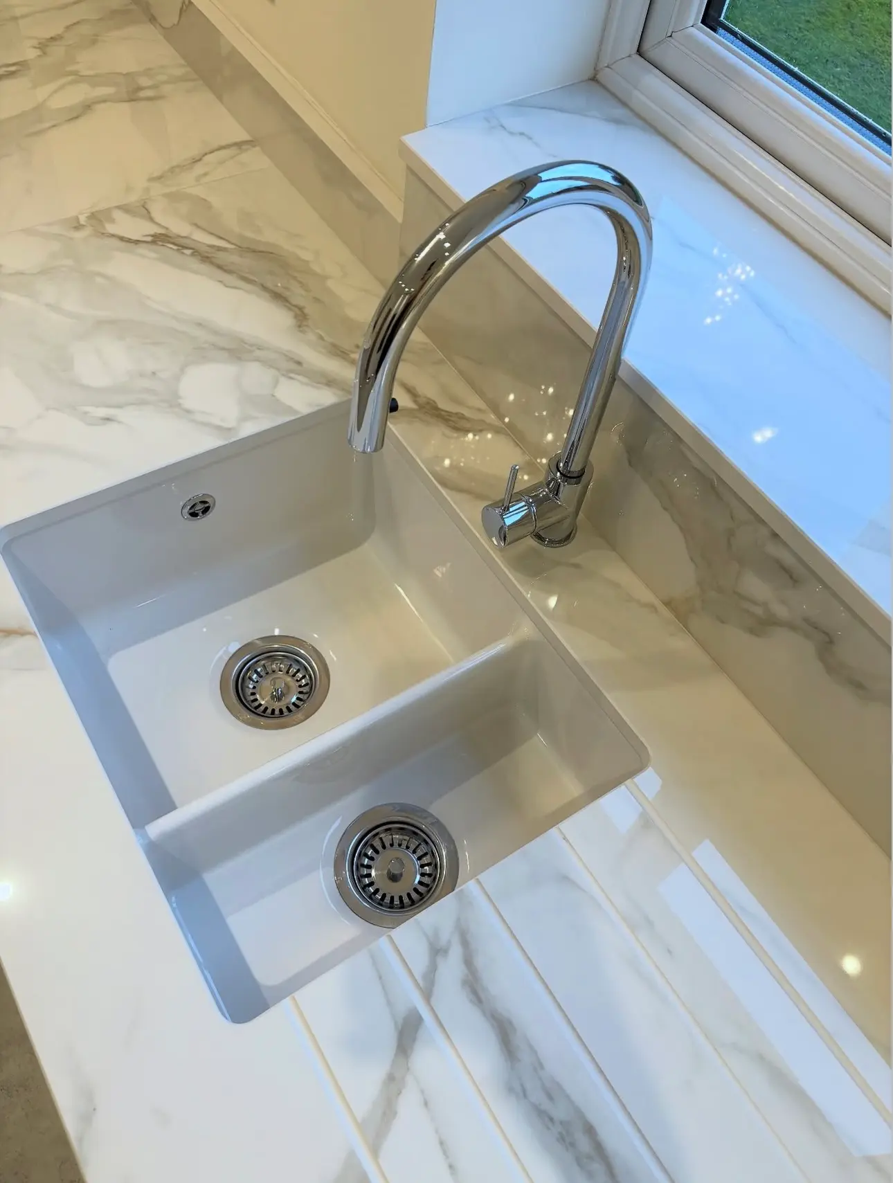 A deep-cleaned kitchen sink and chrome faucet with a mirror-like finish, featuring polished marble countertops and sanitized drain strainers.
