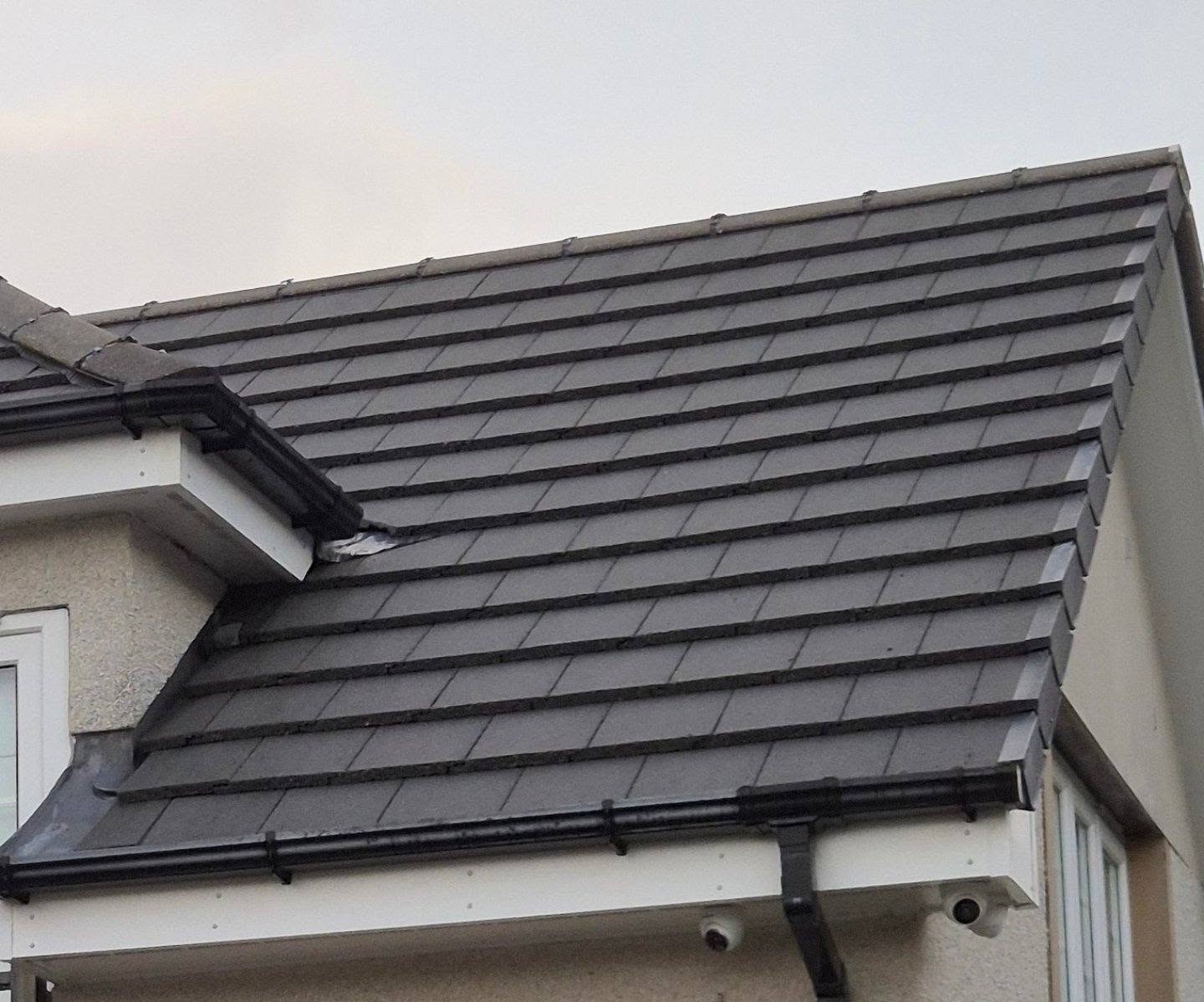 A house with a sloped roof covered in smooth gray tiles and a white exterior. The black gutter runs along the edge. The sky is overcast.
