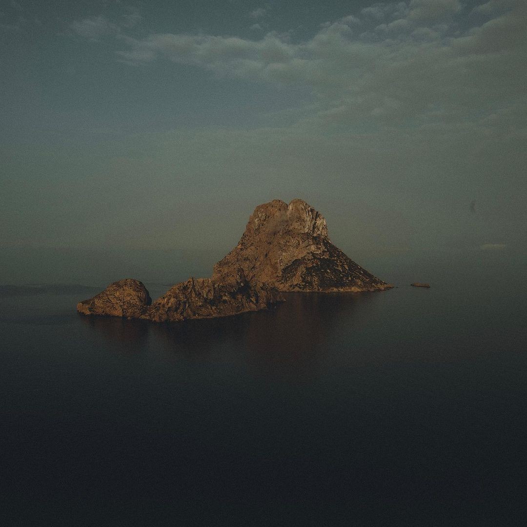 Man sitting in a dimly lit room, wearing a beige shirt and looking contemplative.