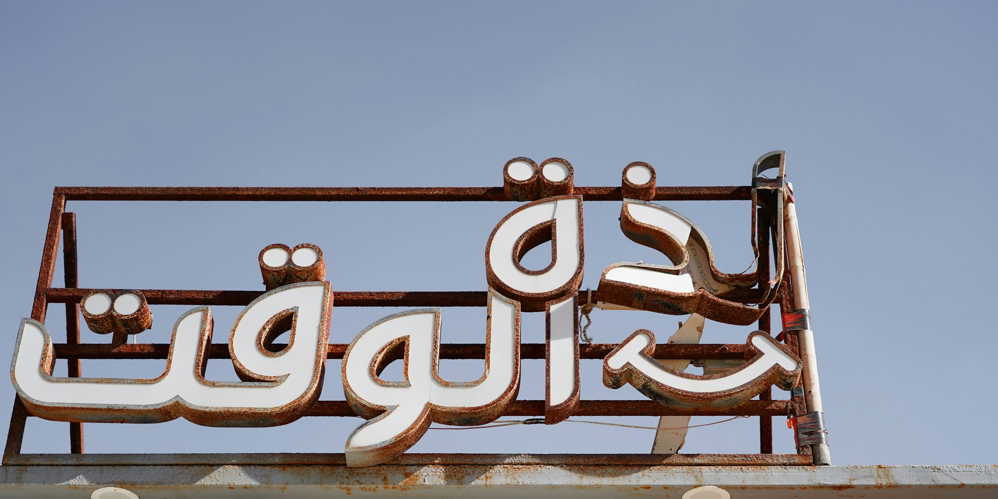 A metal sign with arabic writing on top of a building