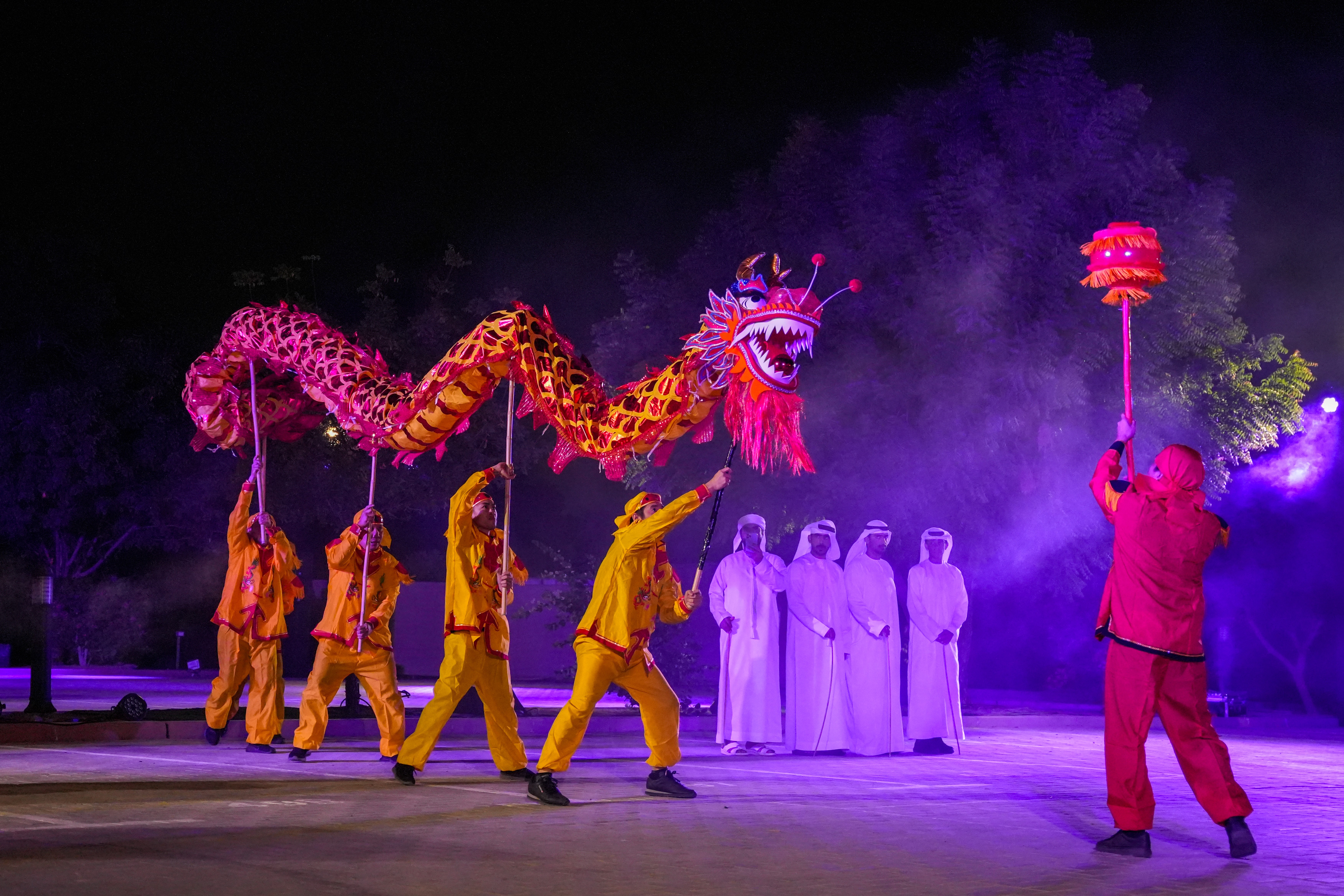 Male scientist in a white lab coat standing confidently in a modern hydroponic lab with pink grow lights and rows of leafy greens.