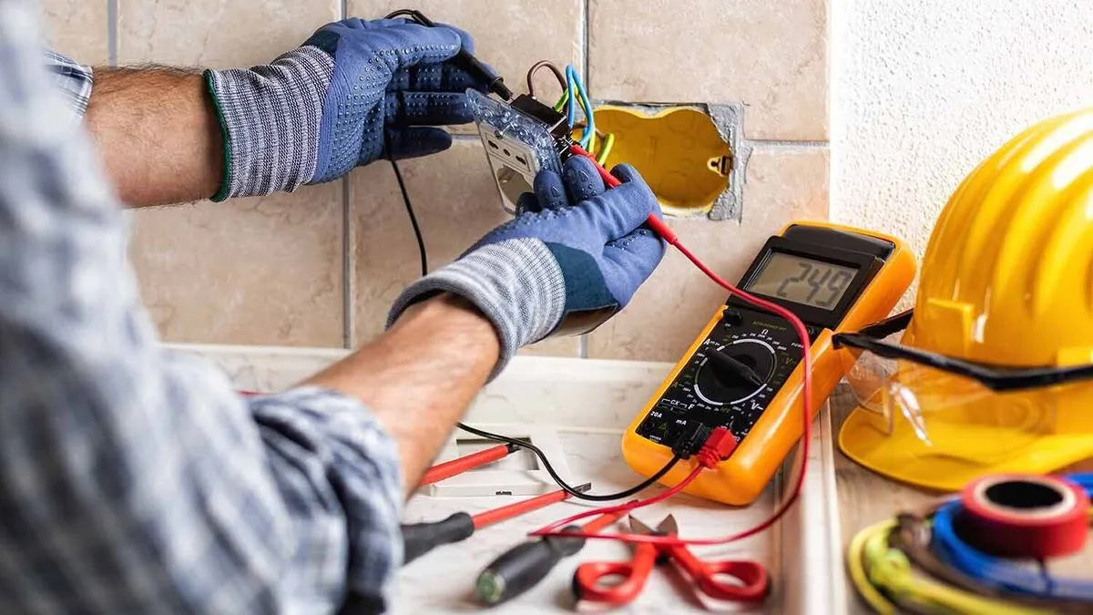 An electrician working on a wall socket with wires exposed.