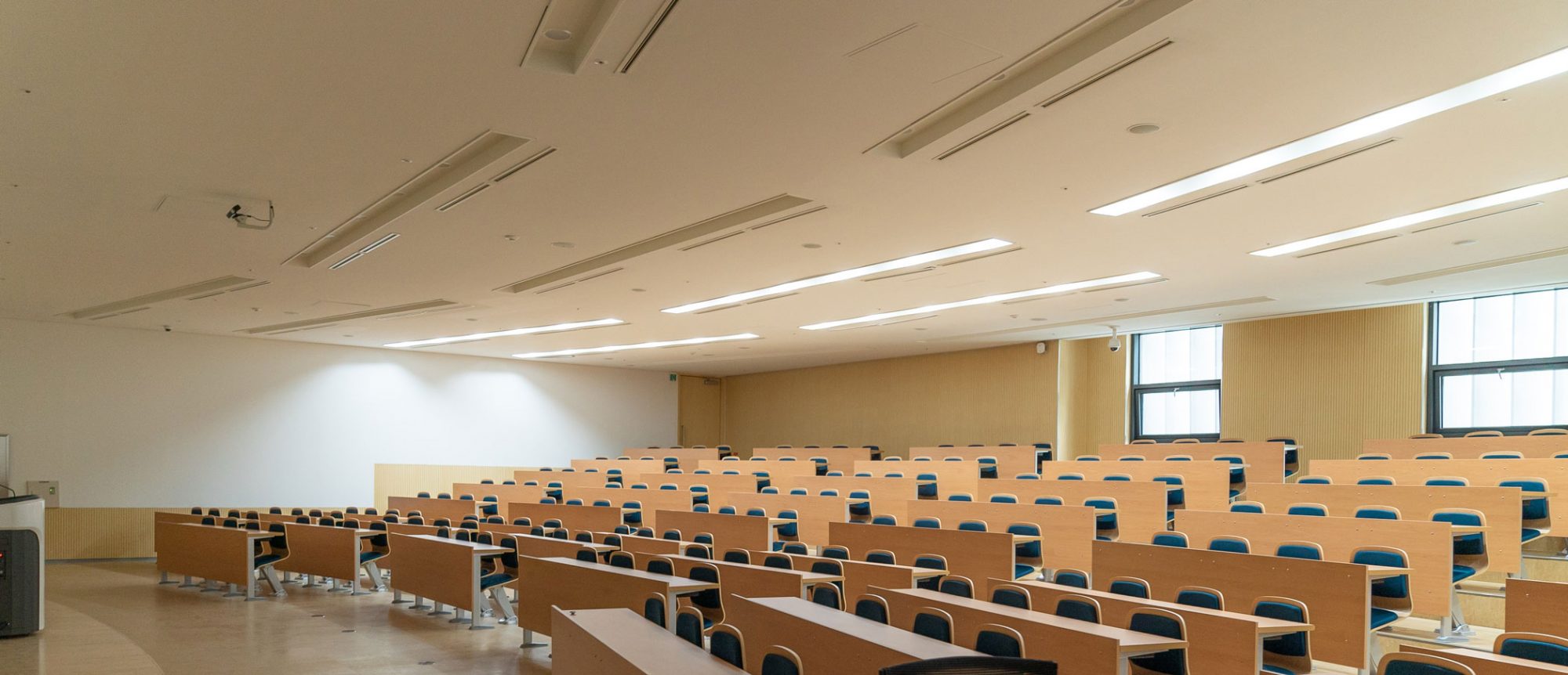 A spacious room with rows of empty chairs, bright lights, and large windows along the walls.