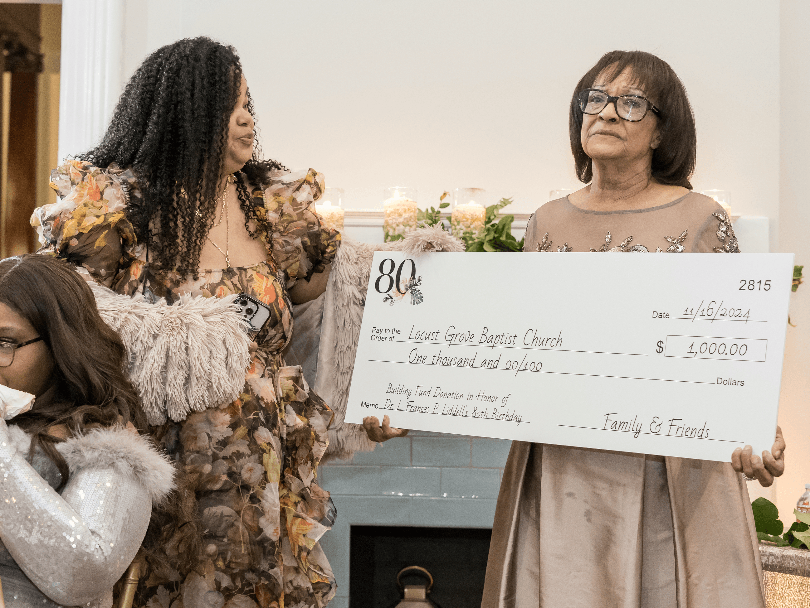 woman in floral gown is presenting her mother with a large sized printed check