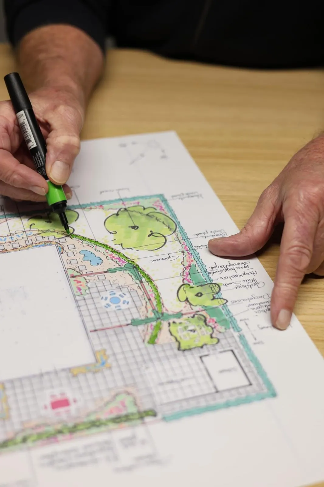 Handen tekenen met marker op ingekleurd tuinontwerp op tafel, schetsfase van tuinontwerp en advies in Friesland