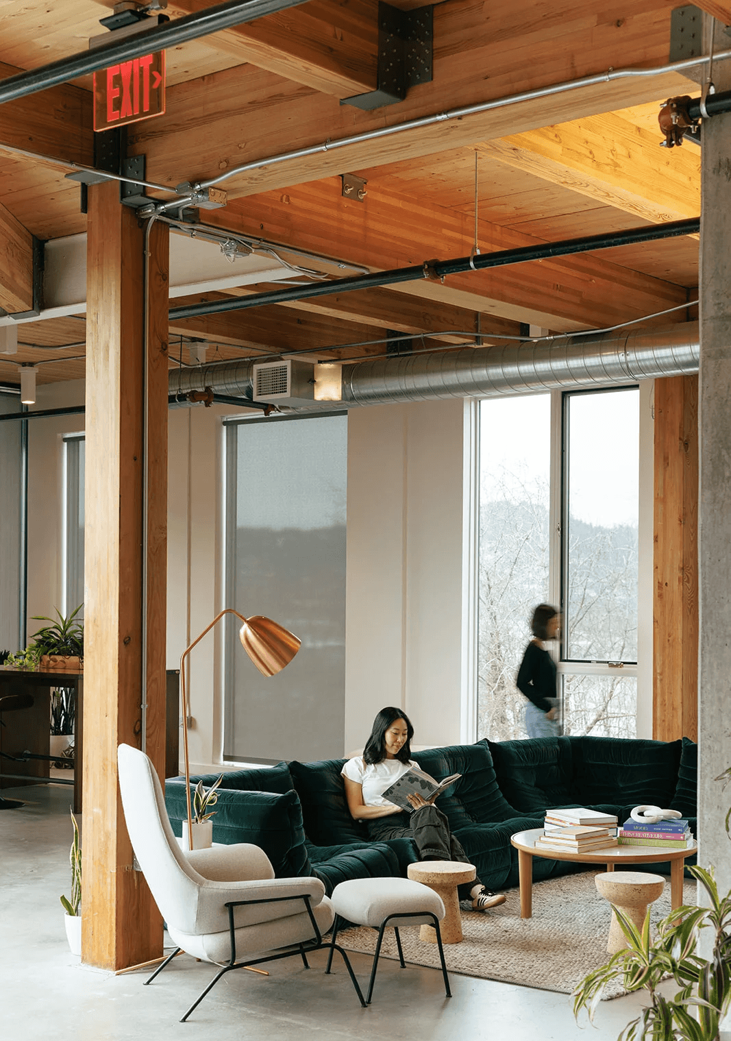 Bright office lounge with a green sofa and a person working by the window