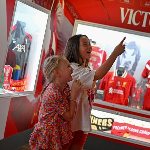 שתי ילדות צעירות מצביעות בהתרגשות ומחייכות כשהן מביטות בתצוגה של מזכרות וחולצות כדורגל במוזיאון.