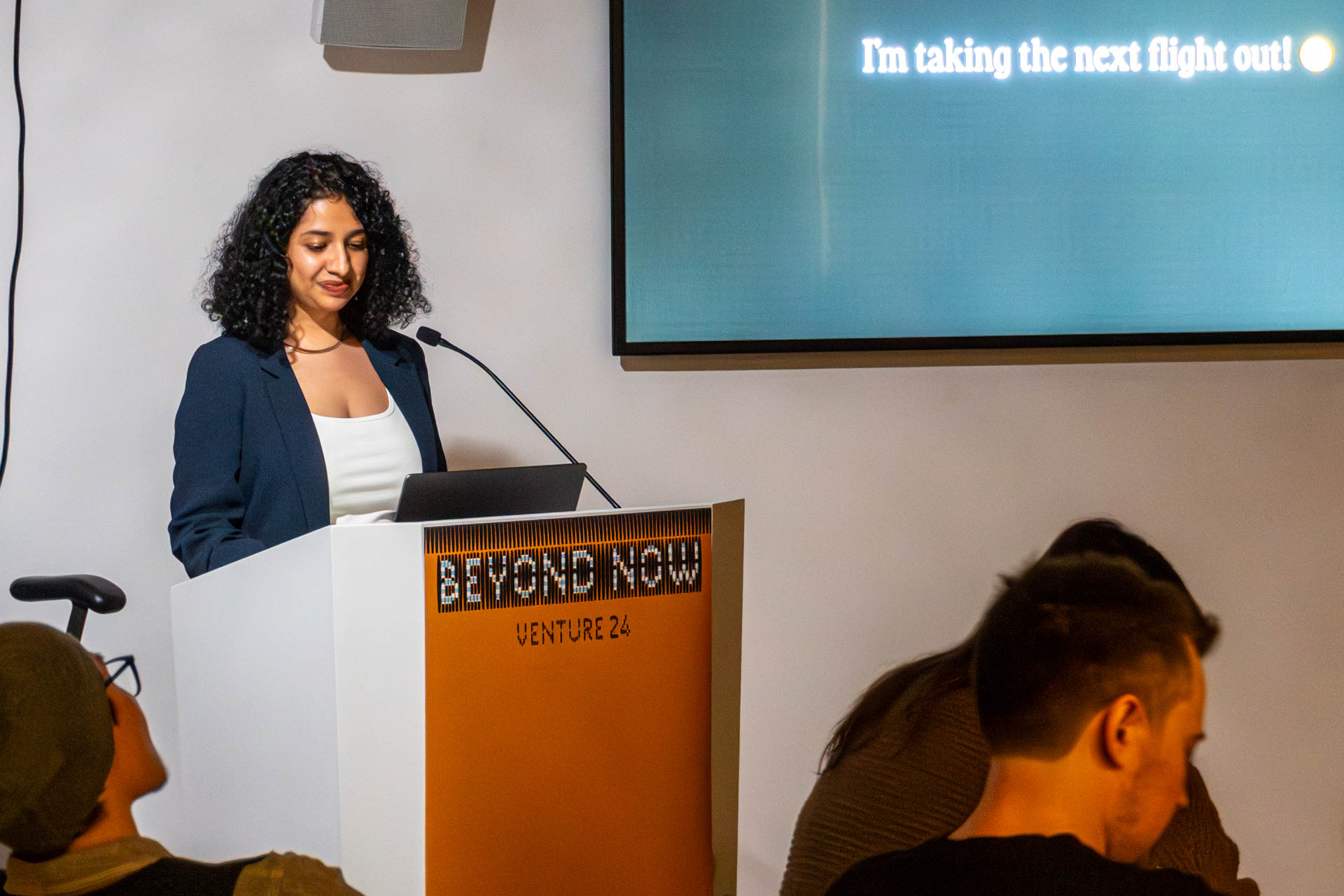 A lady at the podium giving a presentation to a class.
