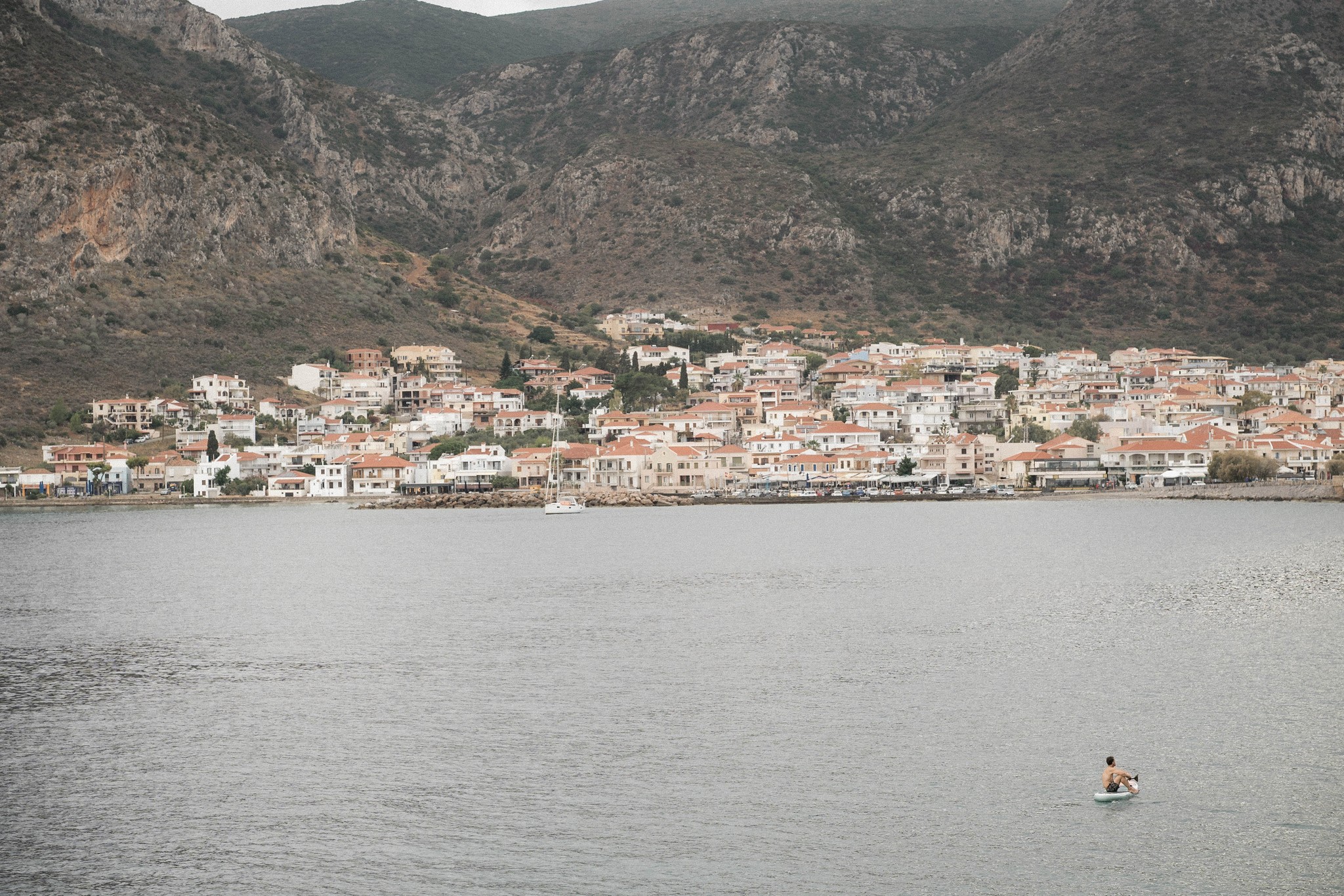 man alone on paddle in front of a montainous mediterranean village