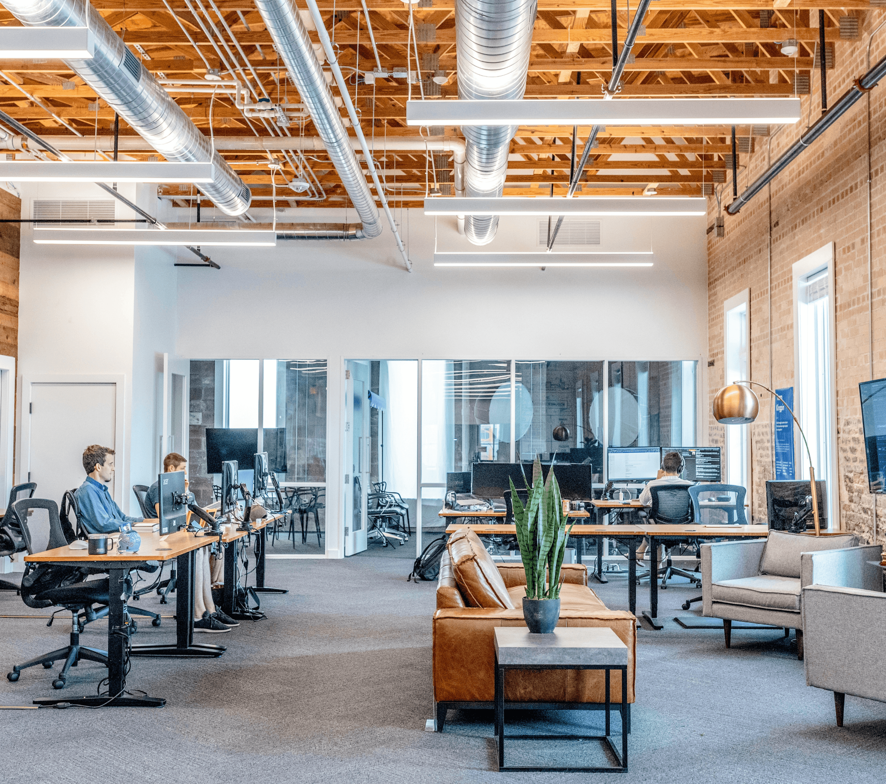 Bild eines modernen Großraumbüros im Industrial style mit Sofas und Schreibtischen an denen mehrere Menschen gerade arbeiten