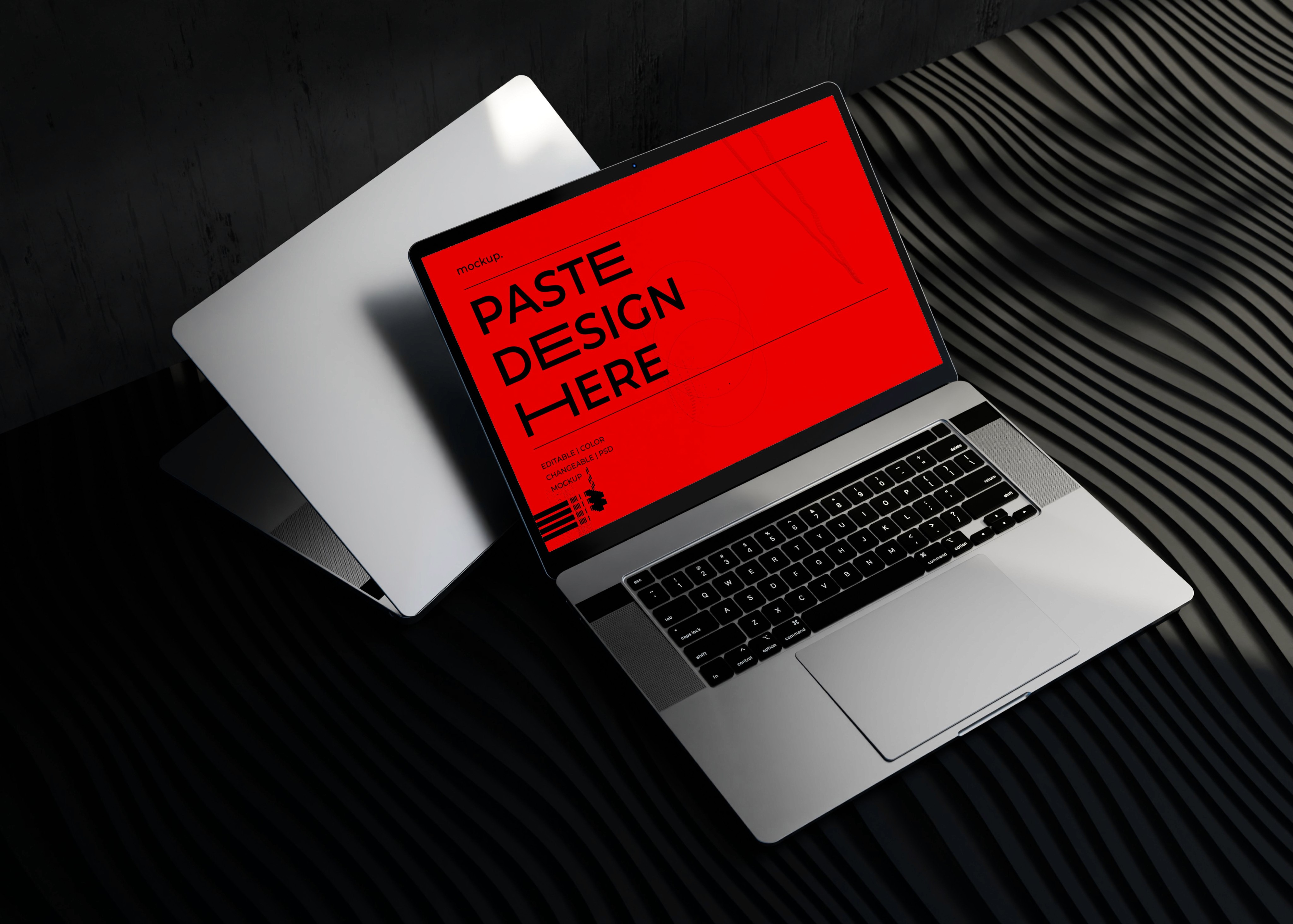 Open silver laptop mockup on black fabric with a red “Paste design here” screen.