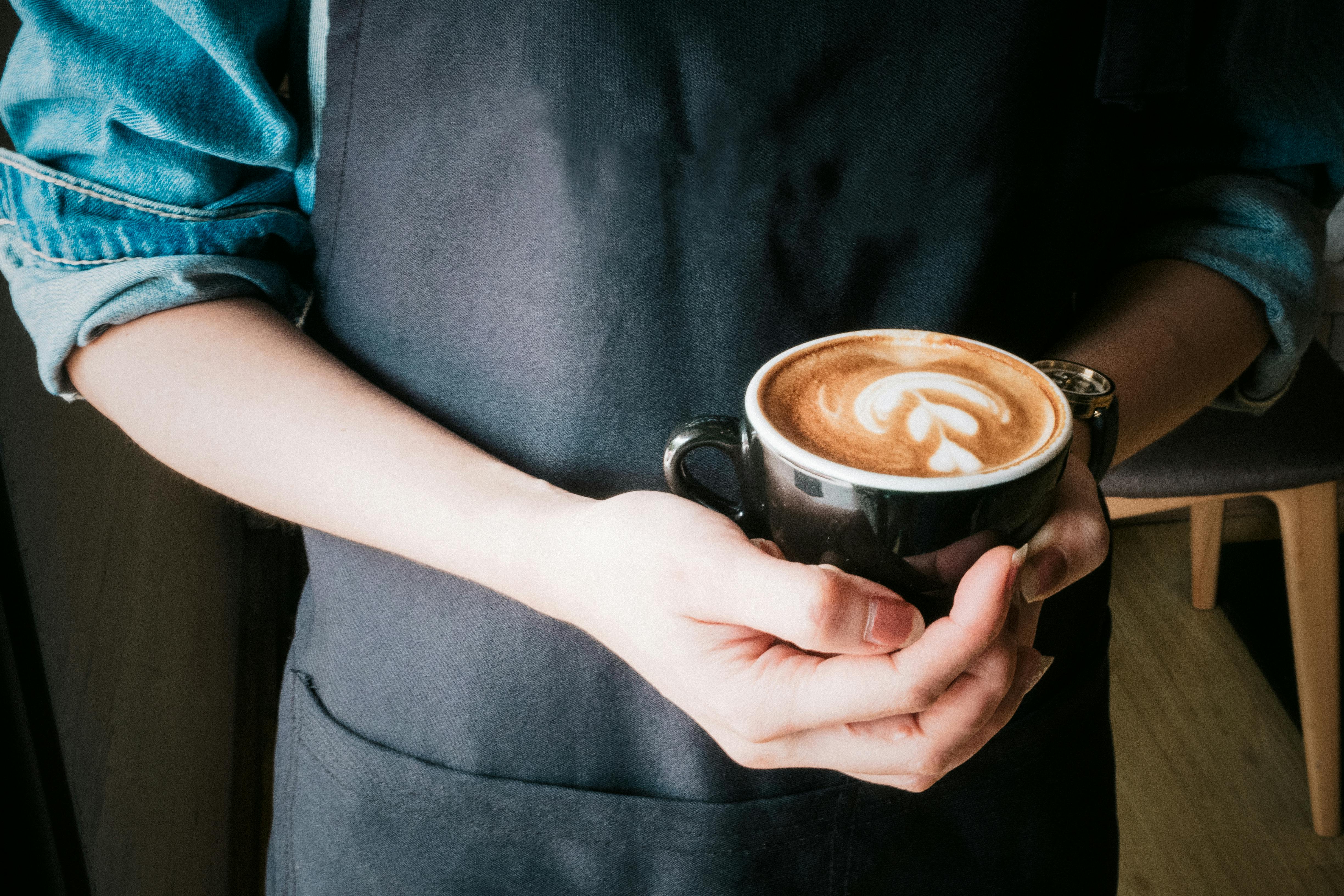 Persona sosteniendo una taza de cerámica con capuchino