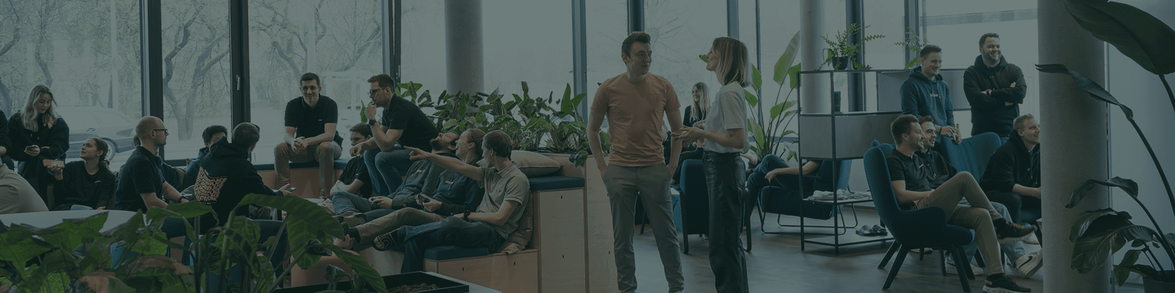 Eine Szene in einer Bürolounge in der viele Menschen sitzen sich unterhalten und an einer Konsole spielen