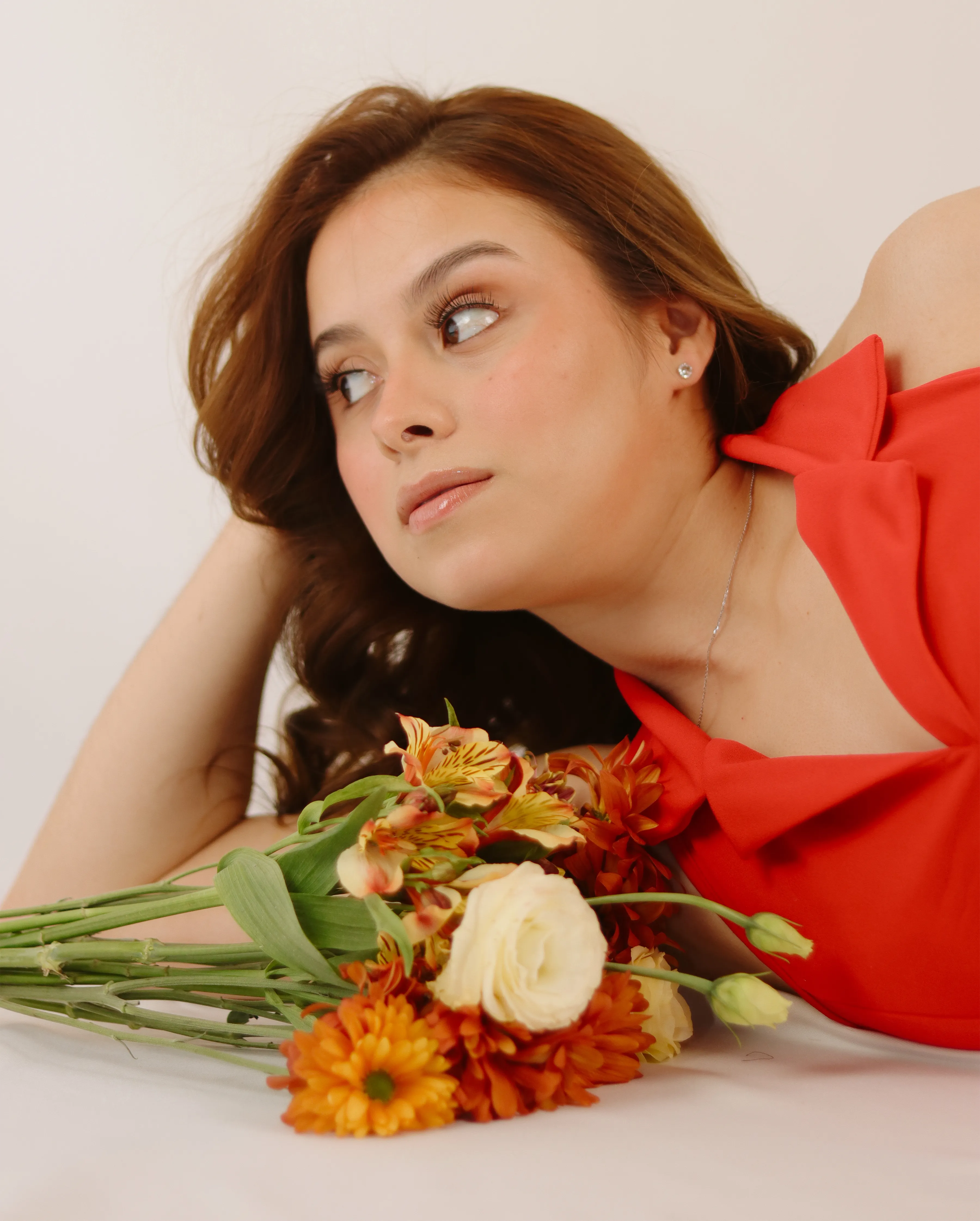 Mujer con vestido rojo mirando al horizonte junto a un ramo de flores