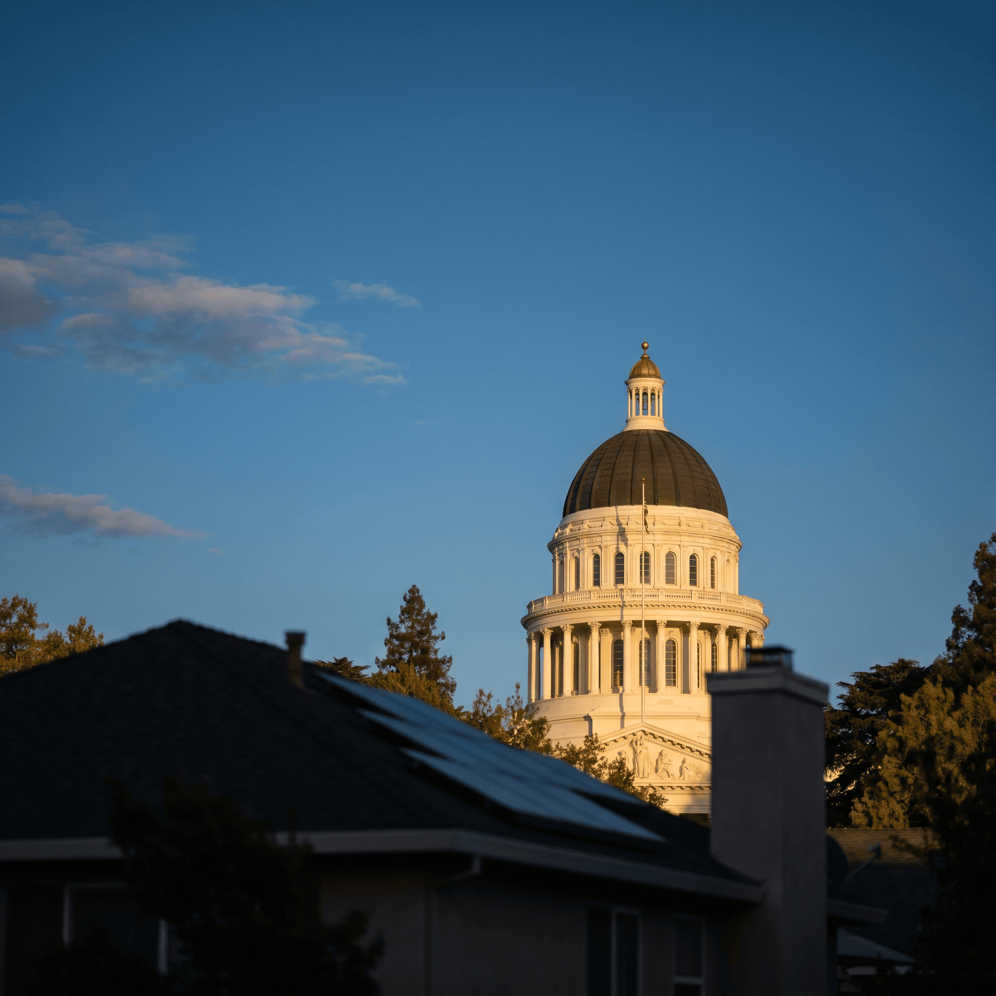 California State Capitol dome in Sacramento at golden hour with a rooftop solar home in soft focus