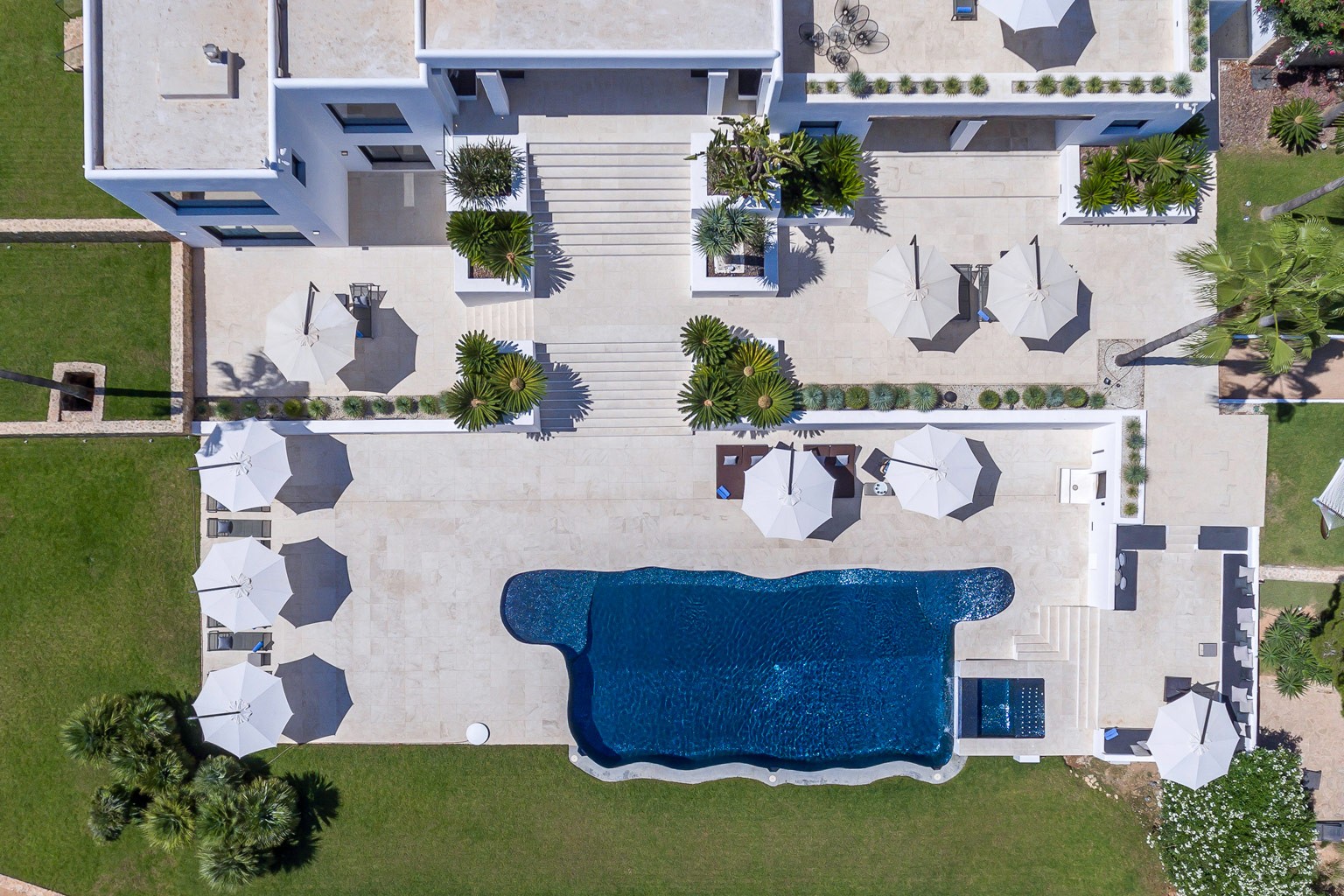 Luftaufnahme eines Küstenresorts mit Pool und Sonnenliegen, umgeben von Bäumen.