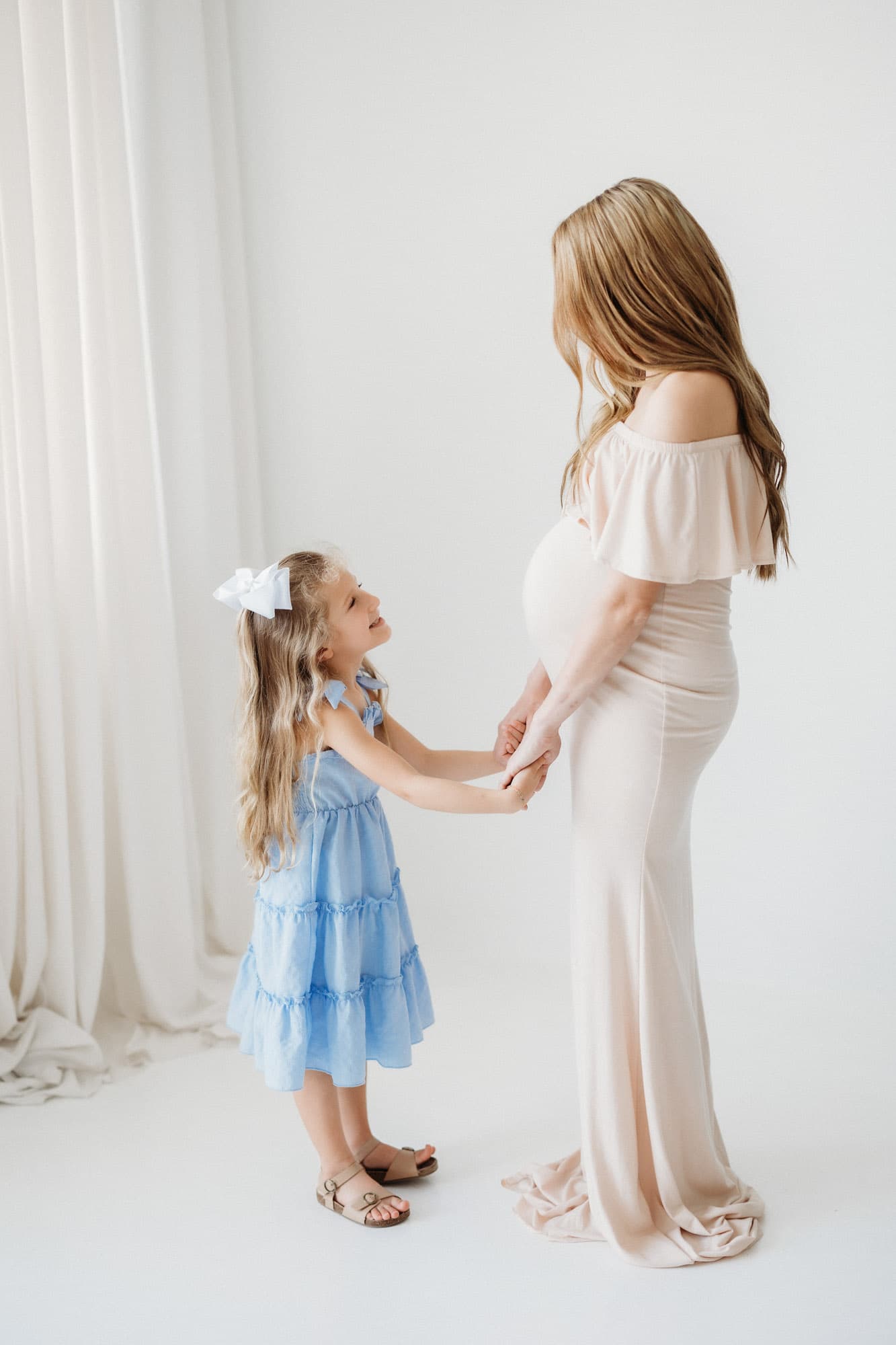 A full-length image of a pregnant woman standing in a beige gown at Revelator Studio in Shreveport, highlighting maternity photography in natural light.