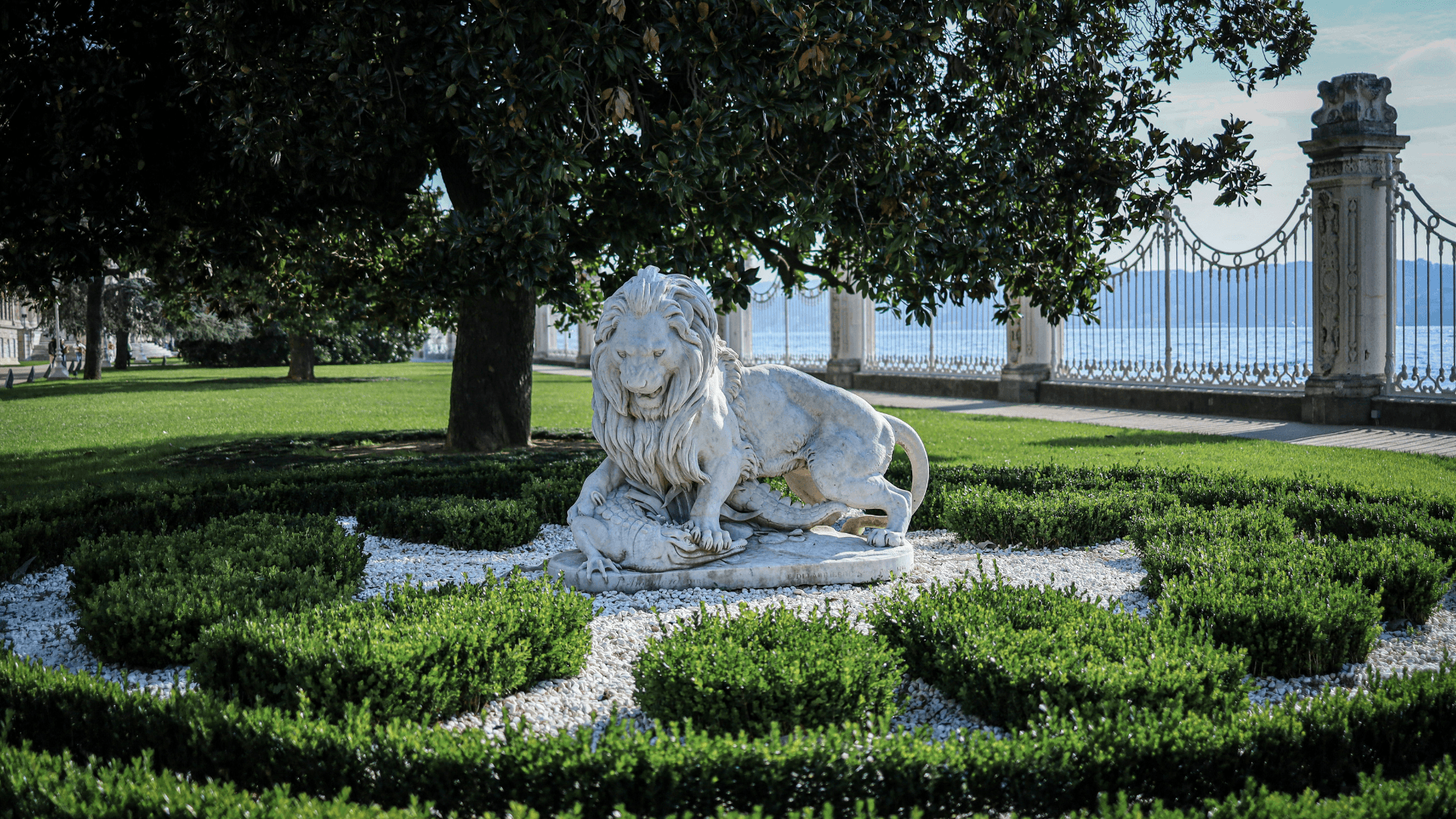Stone lion statue in a historic Ottoman garden overlooking the Bosphorus in Istanbul, surrounded by manicured greenery and palace grounds