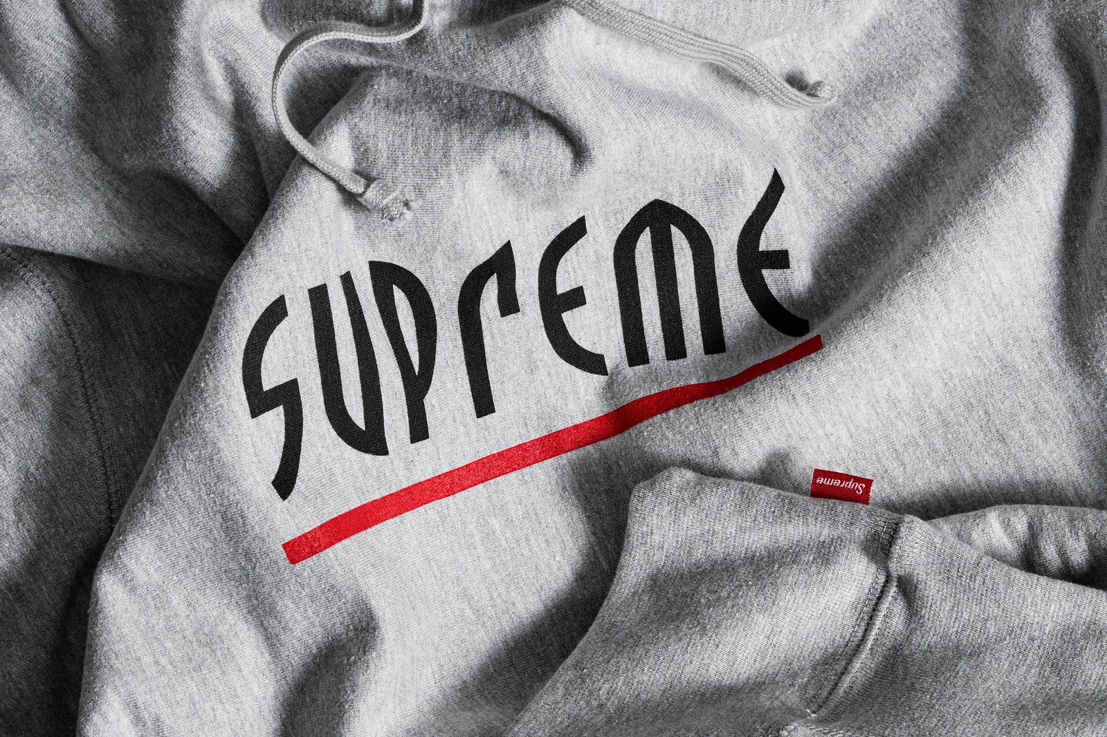 Close-up of fabric on a hoodie featuring the logo "Supreme" in bold, black letters with a red underline.