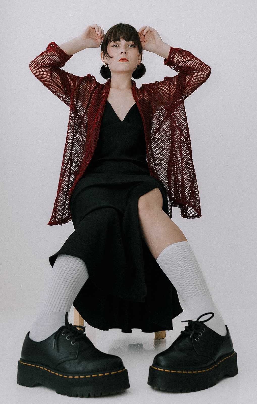 A model sitting in a black dress, wearing white socks and platform shoes, with a red mesh jacket, during the 90s vintage photoshoot at Revelator Studio in Shreveport.