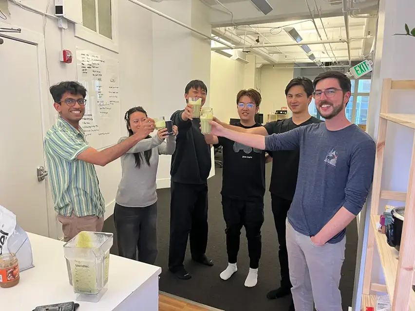Five people raising glasses in a toast inside an office kitchen