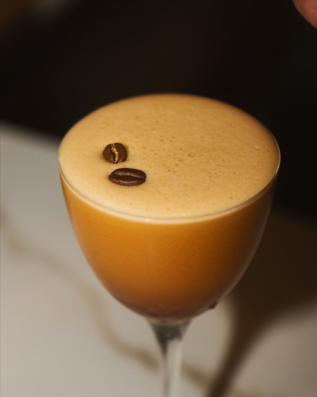 A frothy espresso martini in a stemmed glass topped with two coffee beans.