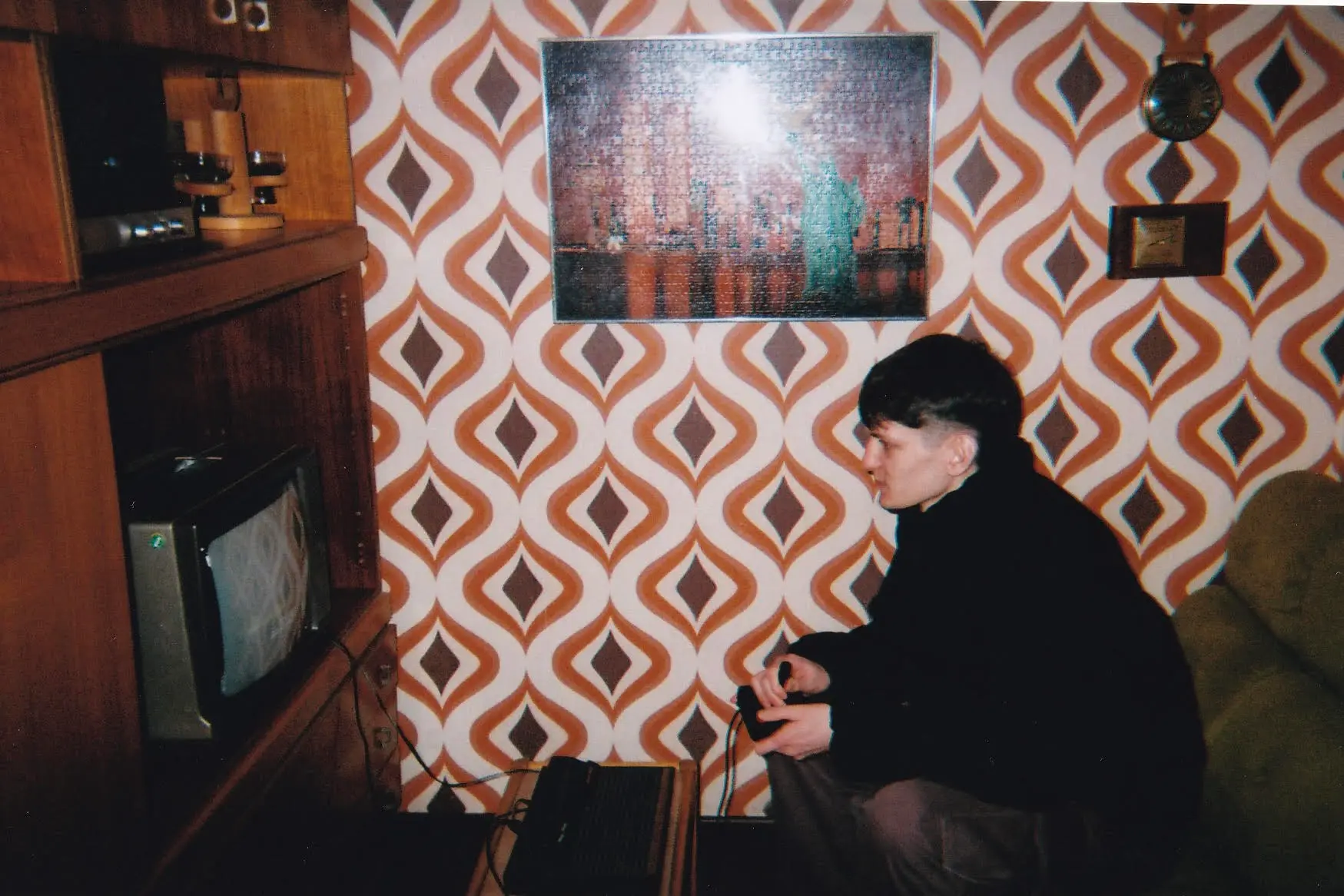 Daniel sitting in a retro themed living room playing a video game on a small television set