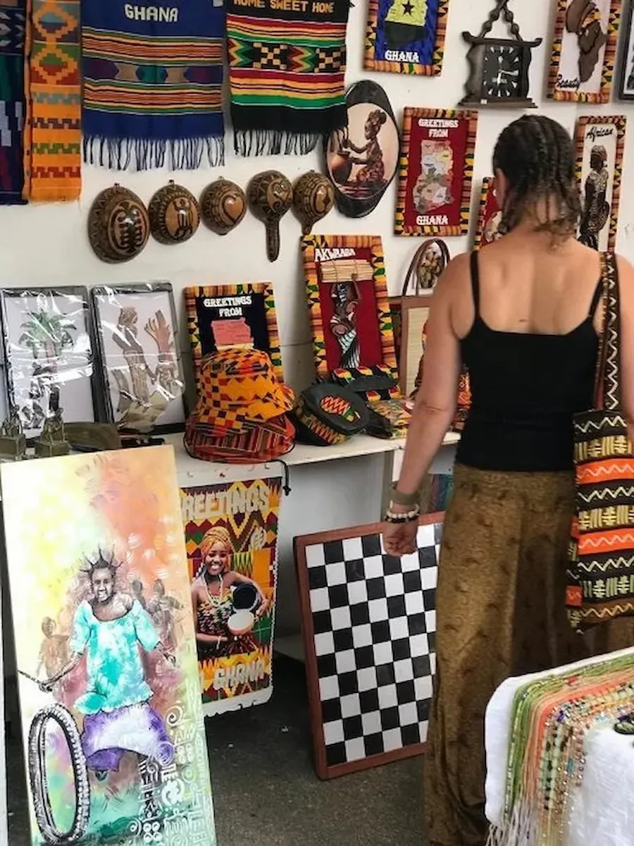 Traveler browsing kente cloth and handmade crafts at a local market, during a BookAfrica Ashanti Heritage Tour.