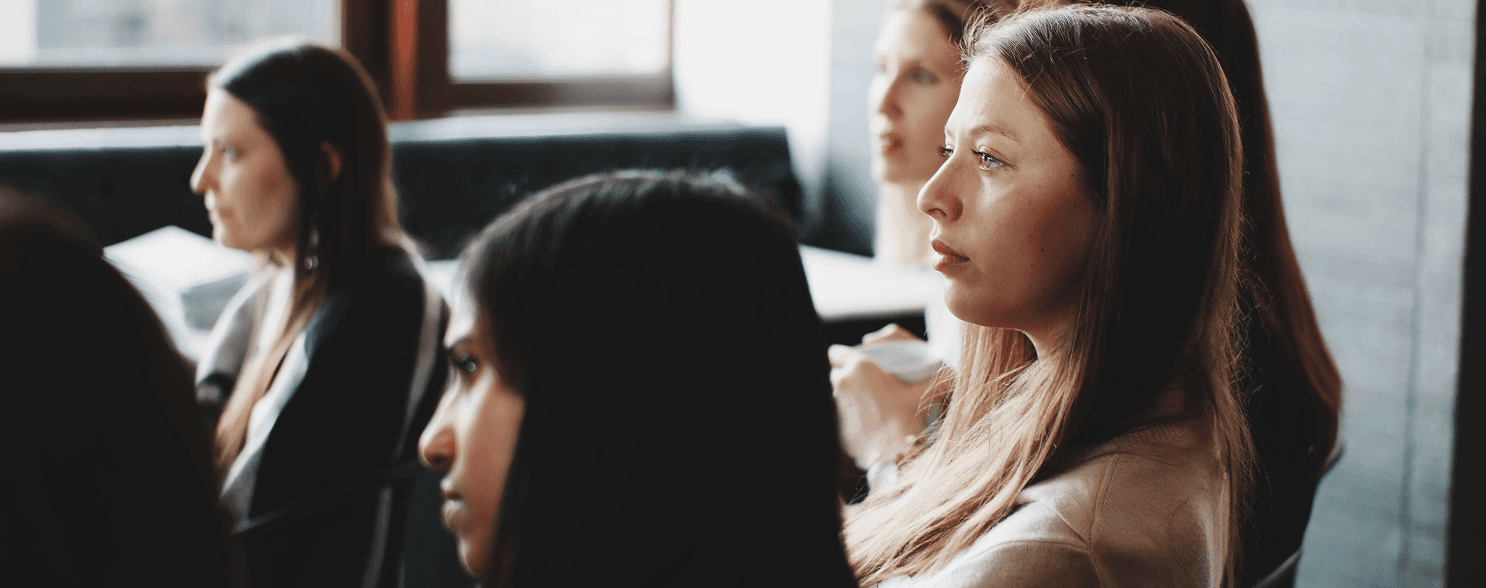 A group of young women engaged in a discussion, with a focus on one woman in the foreground.