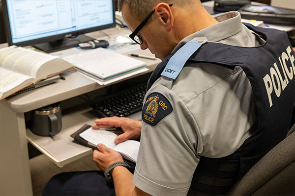 A police officer at a station desk manually handwriting notes into a paper notepad.