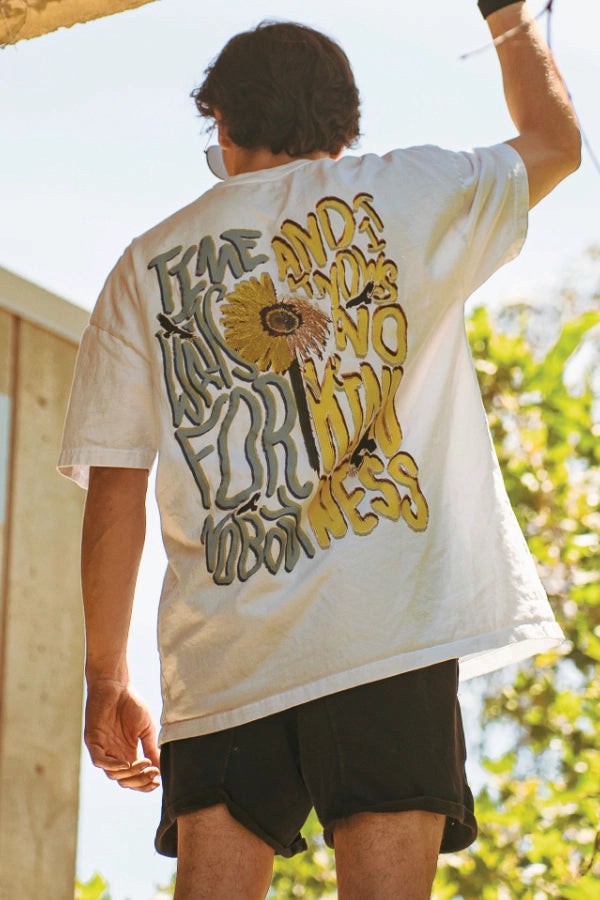 Parkour athlete wearing a white t-shirt with a sunflower design and text on the back, standing outdoors.