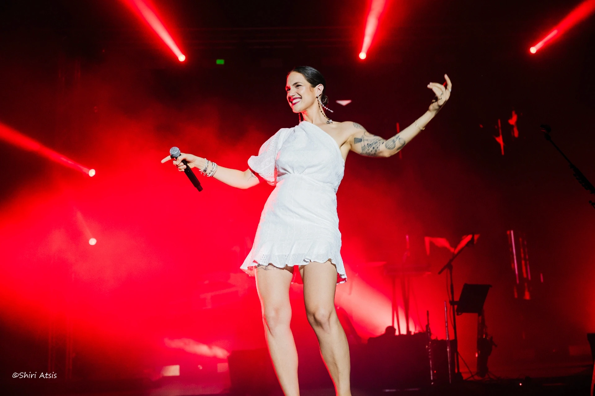 מרינה מקסימיליין בלומין בהופעה חיה על רקע תאורה אדומה דרמטית, צילום הופעות מקצועי של הצלמת שירי עציץ Shiriz – סטודיו לצילום סטילס ווידאו.